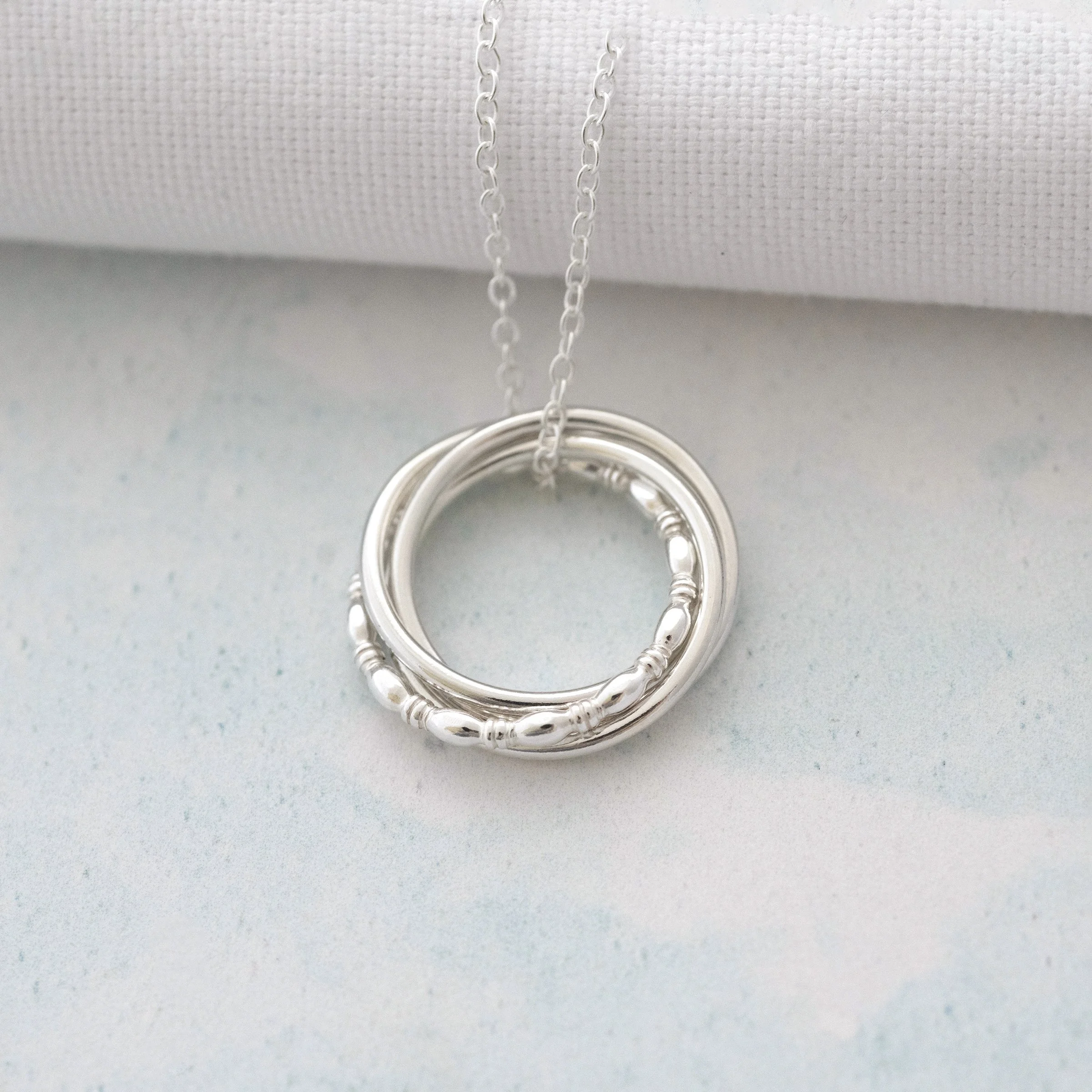 A silver circle necklace displayed against a blue background.