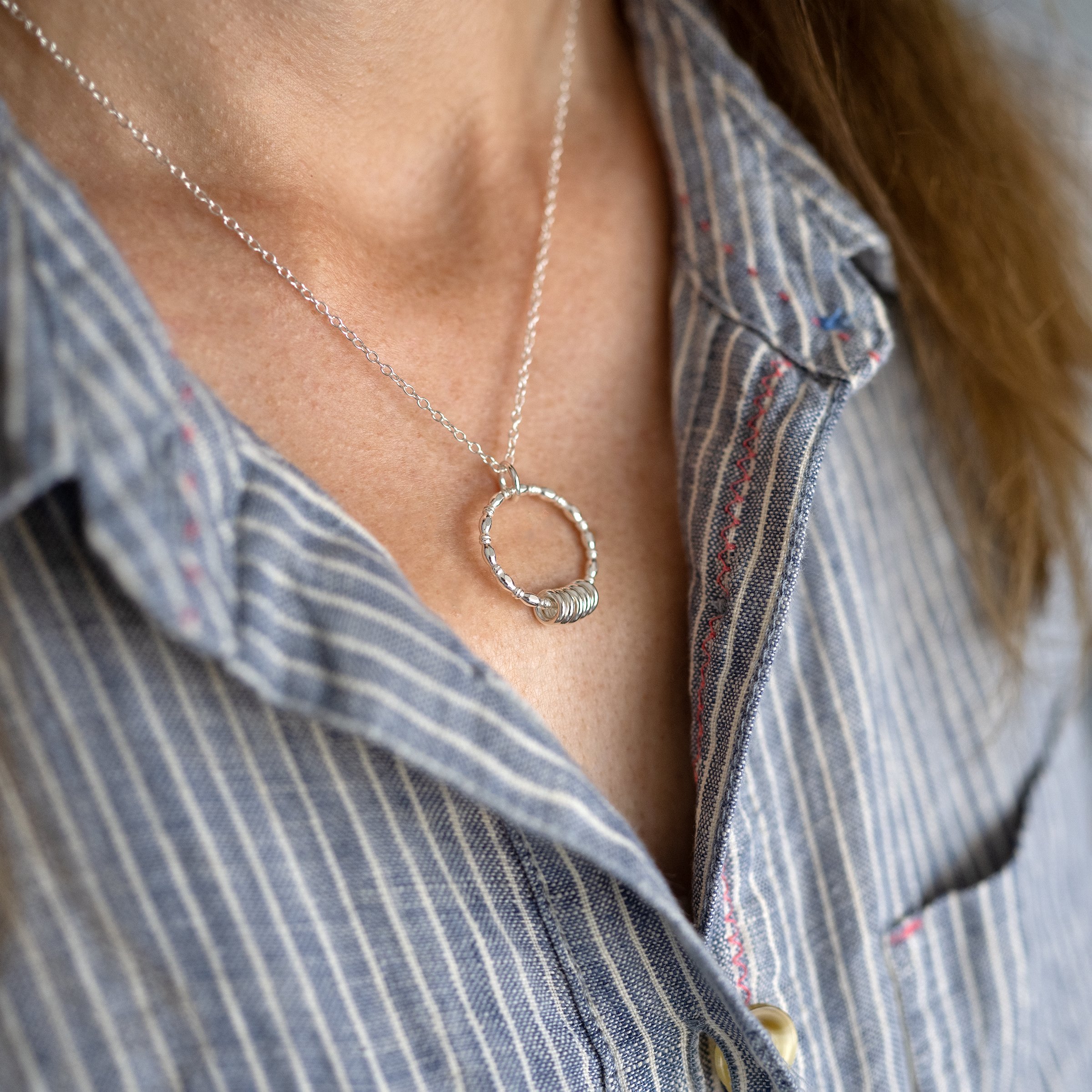 A side view of a person wearing a silver five ring necklace against a blue and white striped dress.