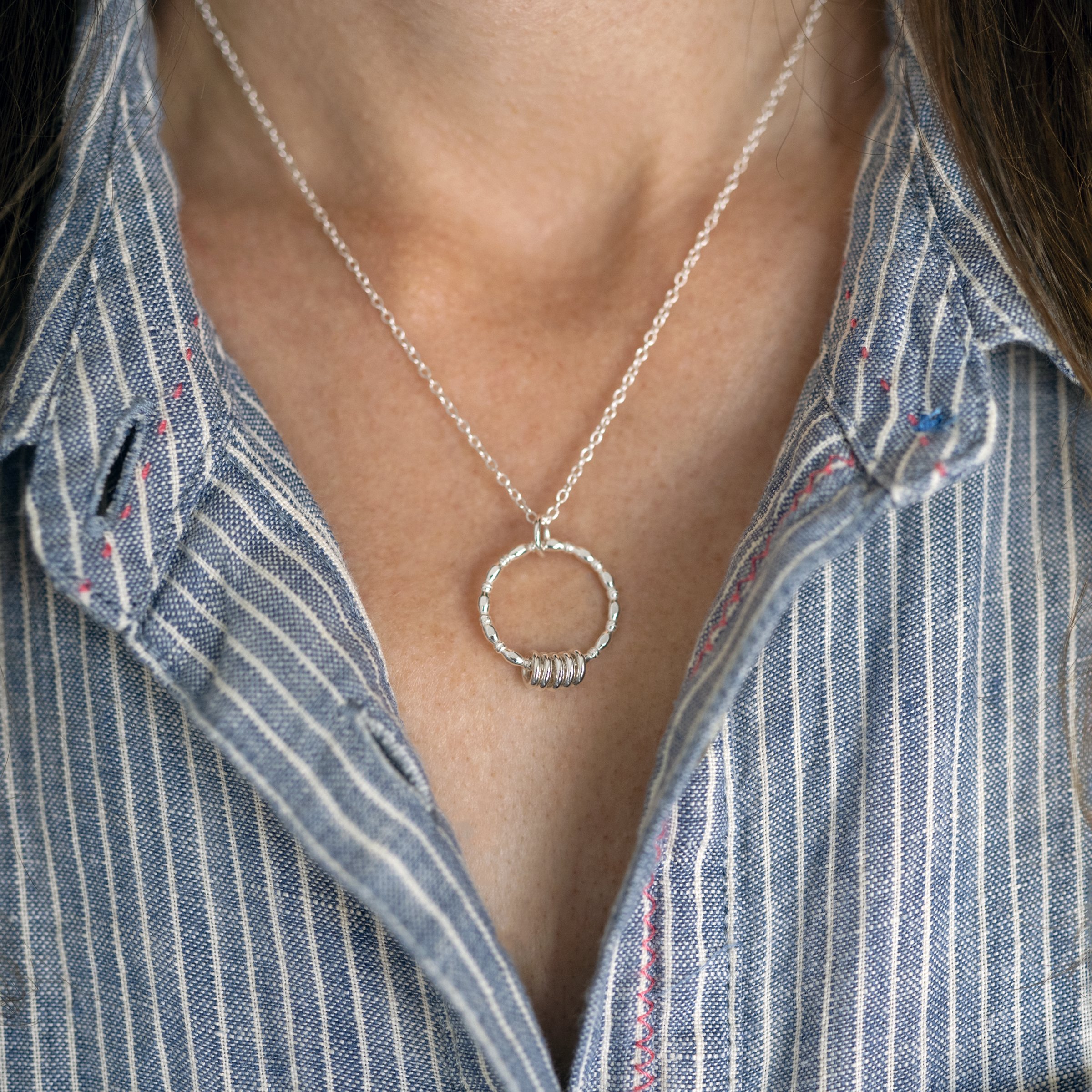 A close up of a person wearing a silver 50th birthday necklace against a blue and white striped dress.