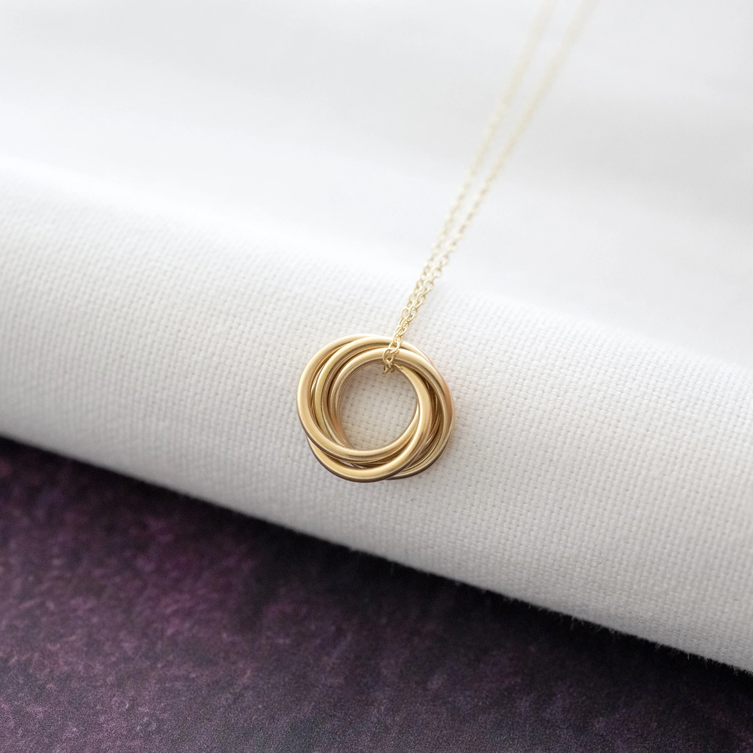 A gold 40th birthday necklace displayed over white material and a purple background.