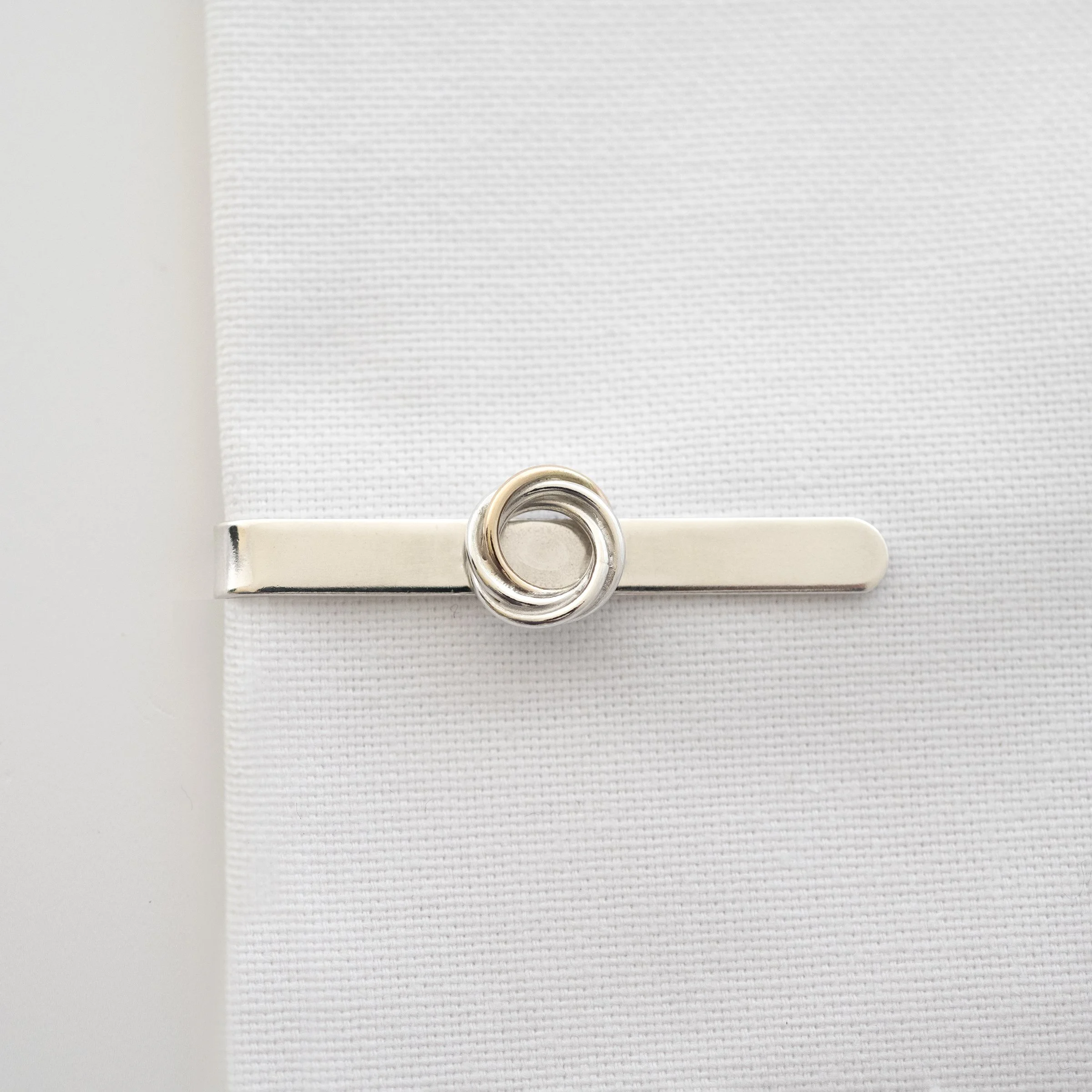 A gold and silver 40th tie clip displayed on white material.