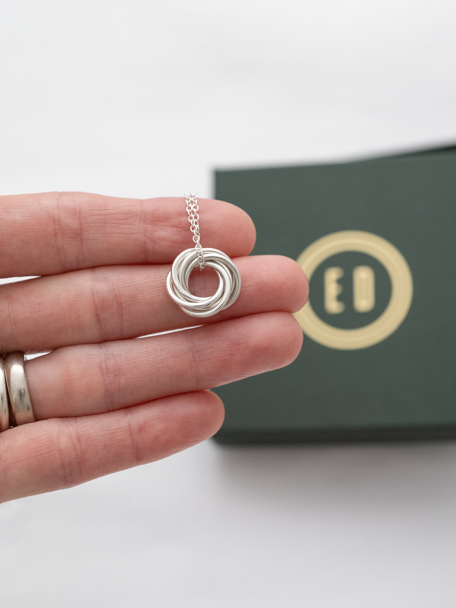 A person displaying a silver six ring necklace over their hand with the jewellery presentation box in the background.
