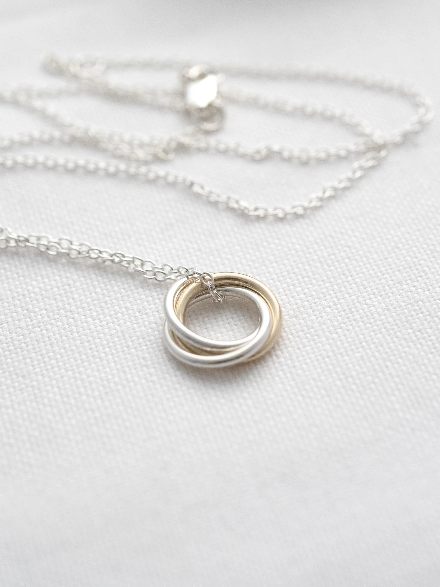 A close up of a handmade 3 ring necklace for a 30th birthday displayed on white material with the chain in the background.