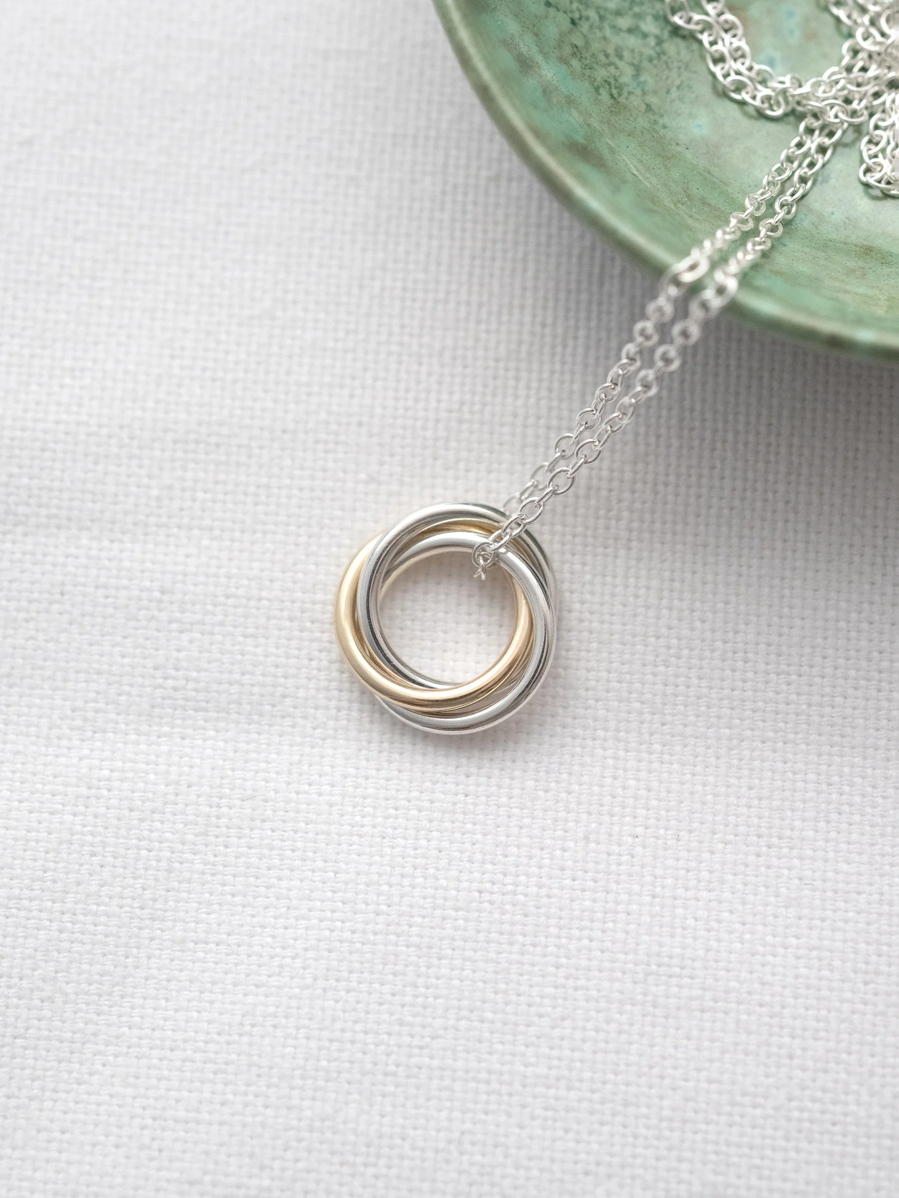 A handmade gold and silver necklace for a 30th birthday displayed on white material with a green jewellery dish in the background.