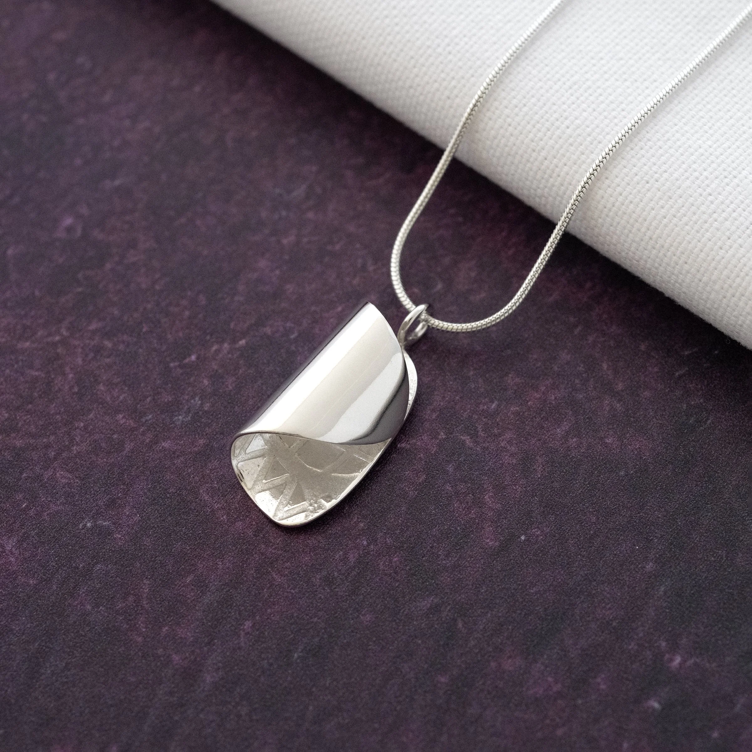A silver curved necklace displayed against a purple backgound.