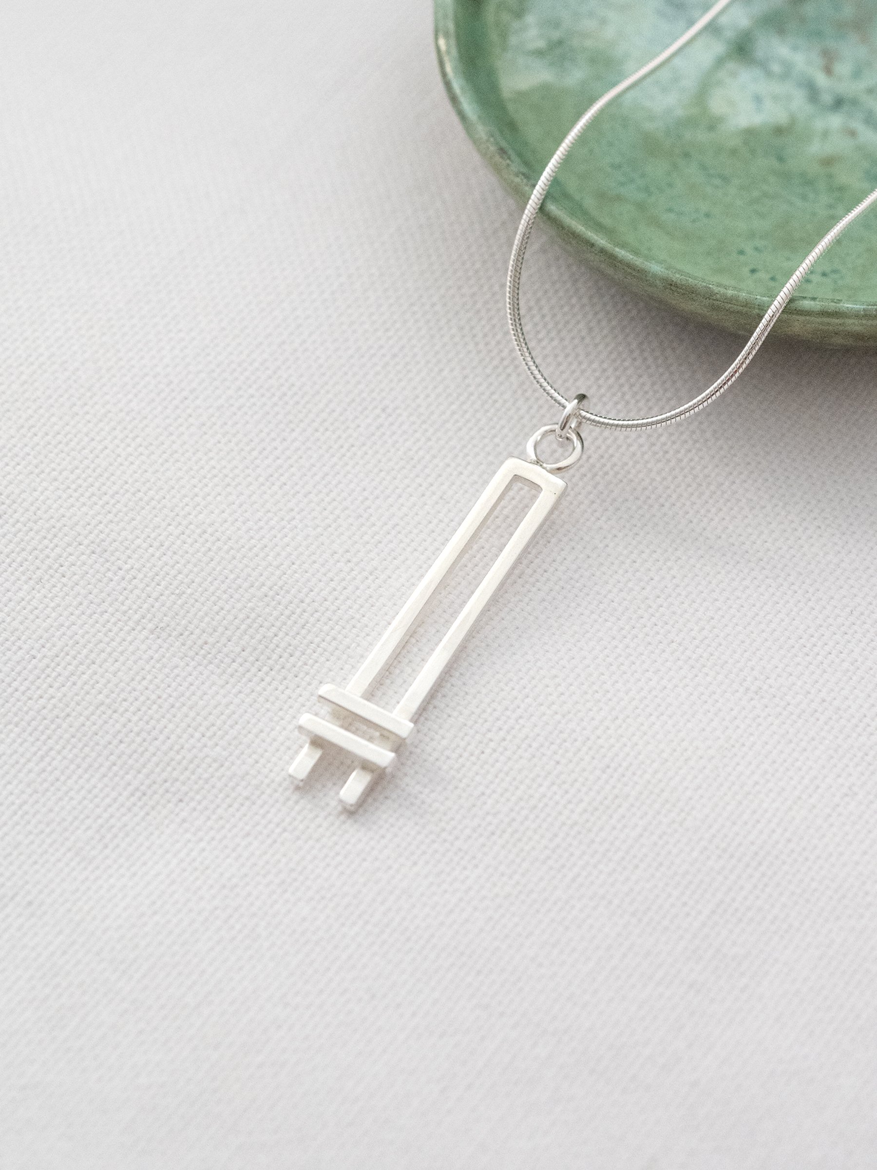 A sterling silver Art Deco style necklace displayed on white material with a green jewellery dish in the background.