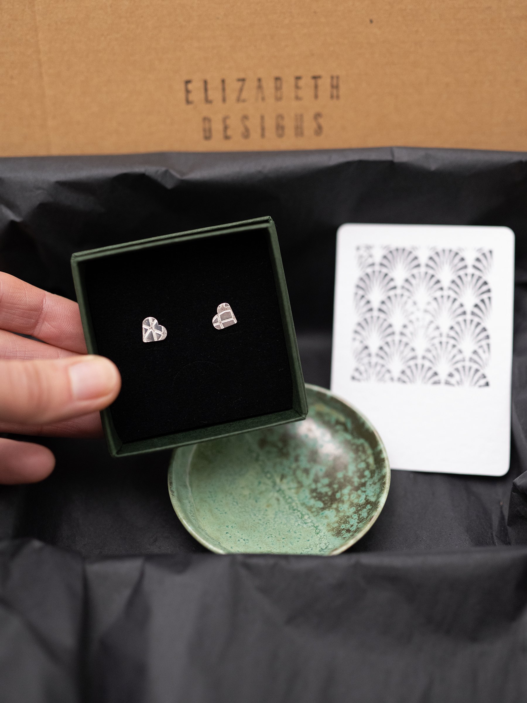 A close up of silver heart stud earrings in a jewellery box presented as a gift set with a handmade jewellery dish.