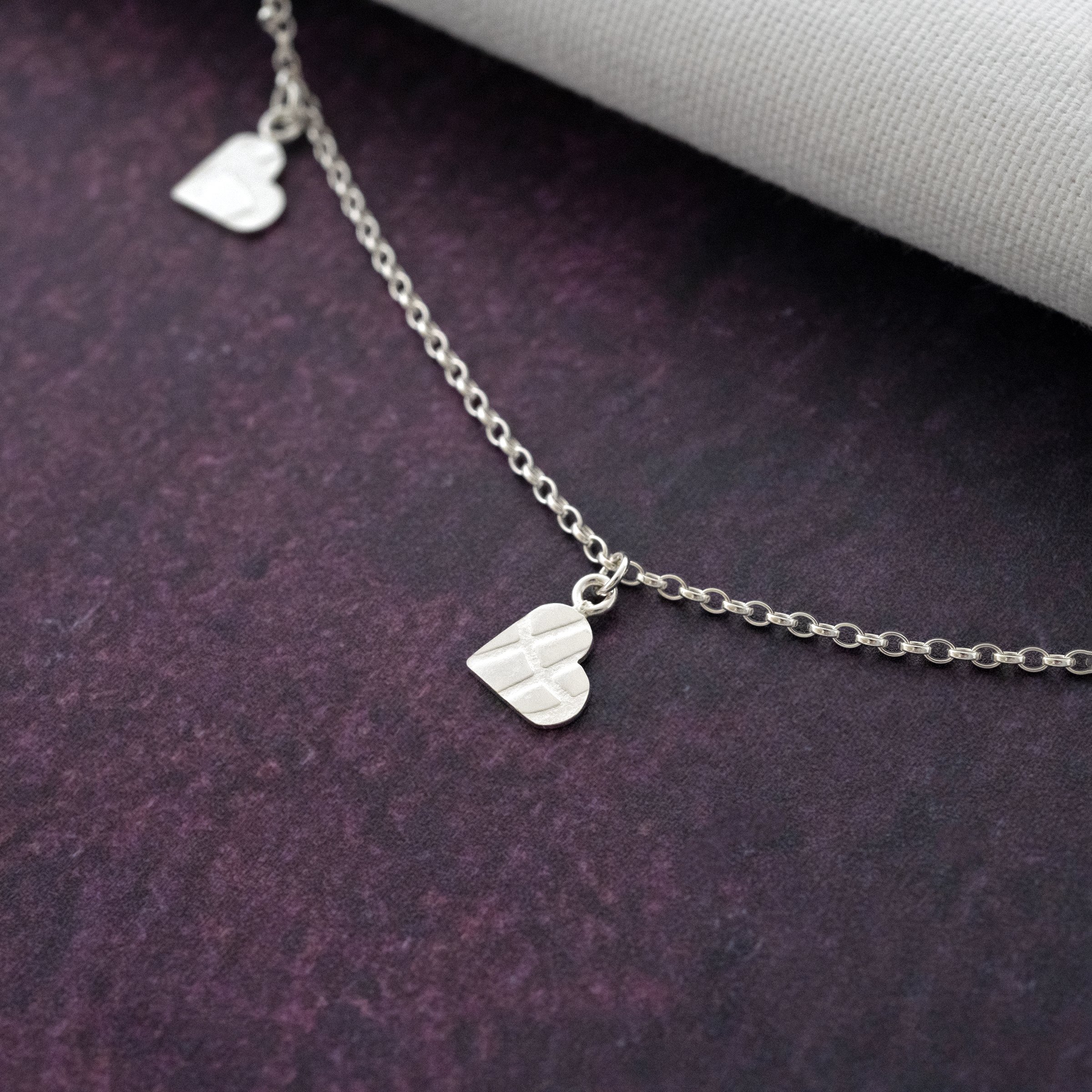 A close up of a textured heart necklace against a purple background.