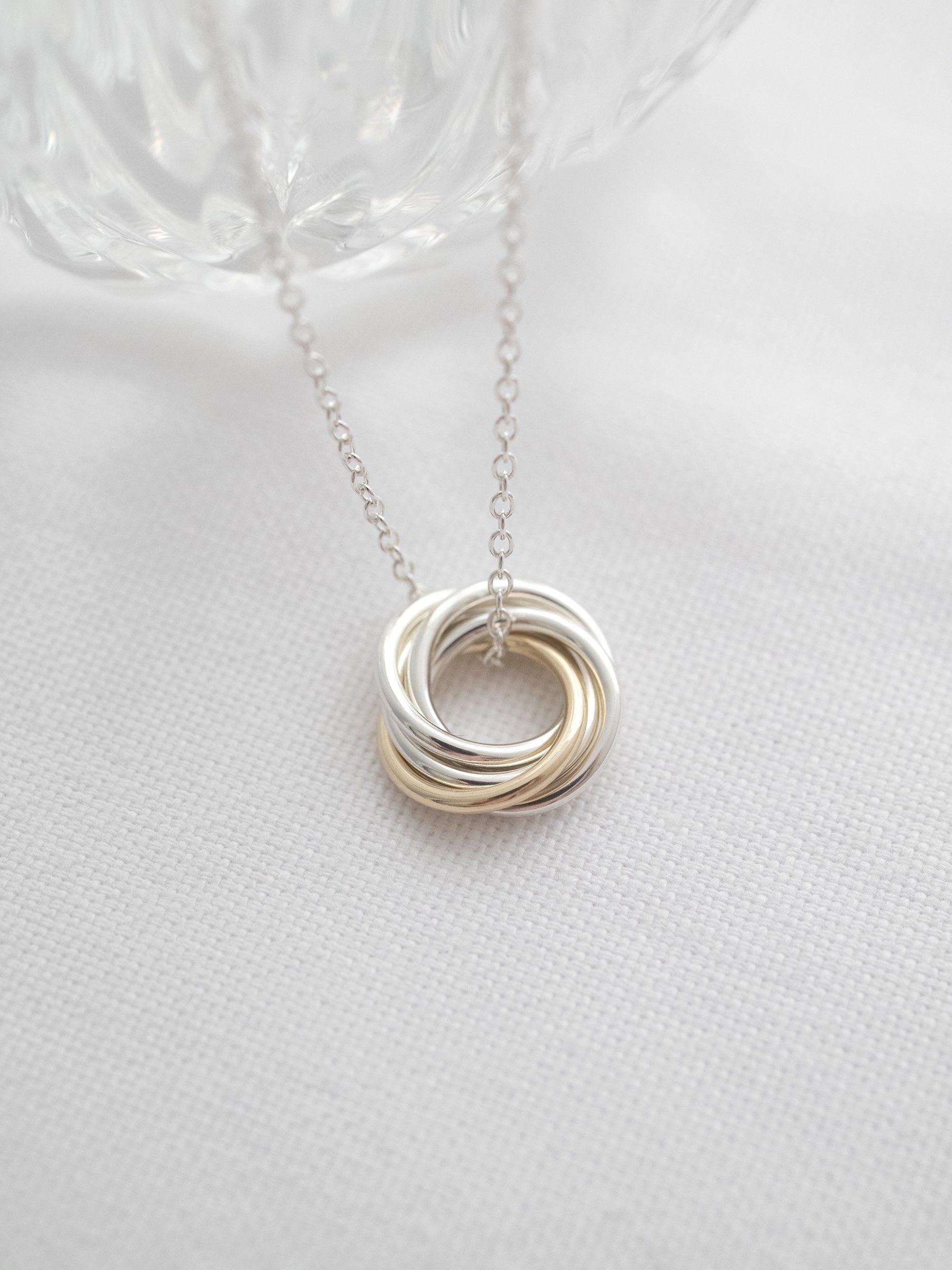 A hallmarked five ring necklace displayed on white material with a decorative glass dish in the background.