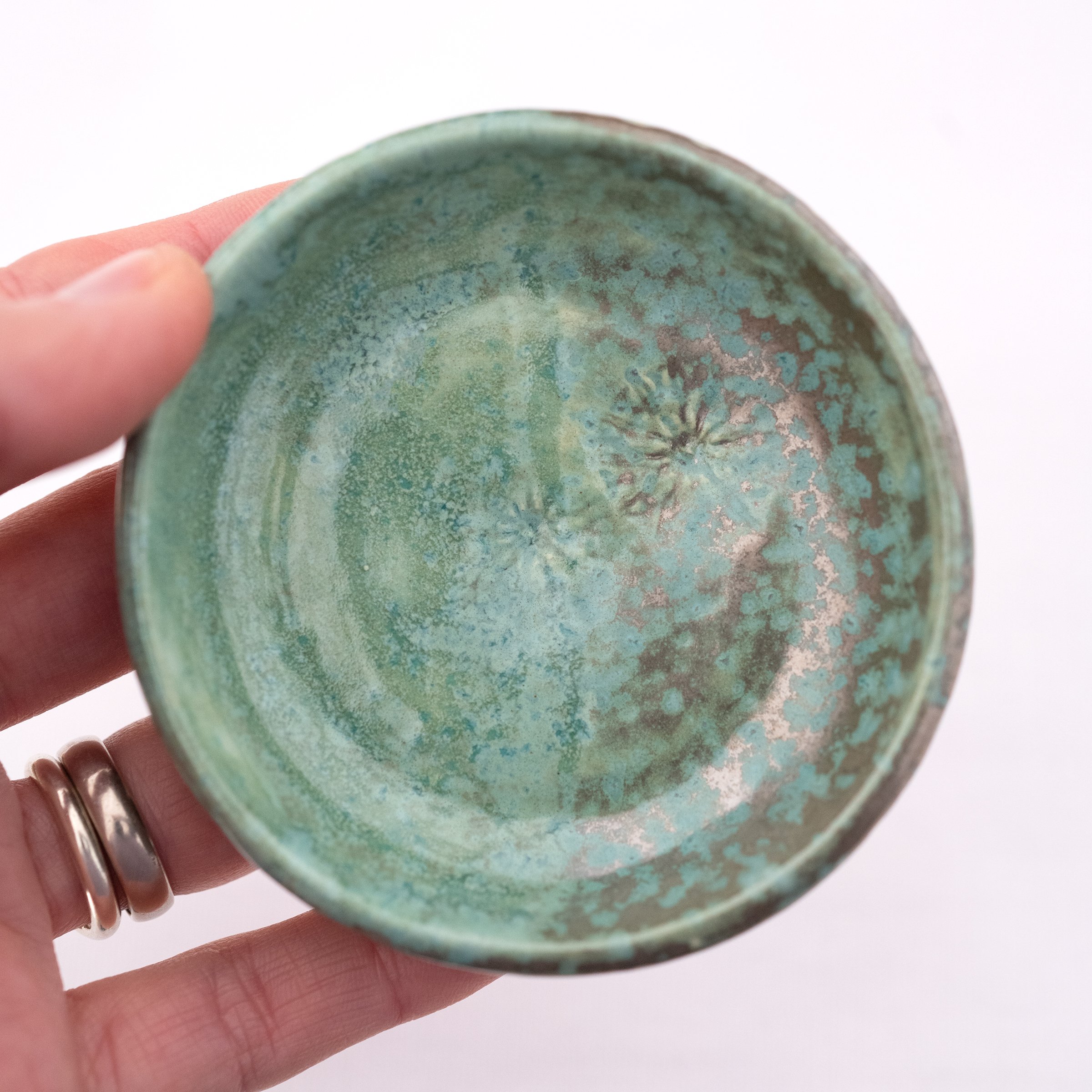 A close up of a person holding a green handmade ceramic jewellery dish.