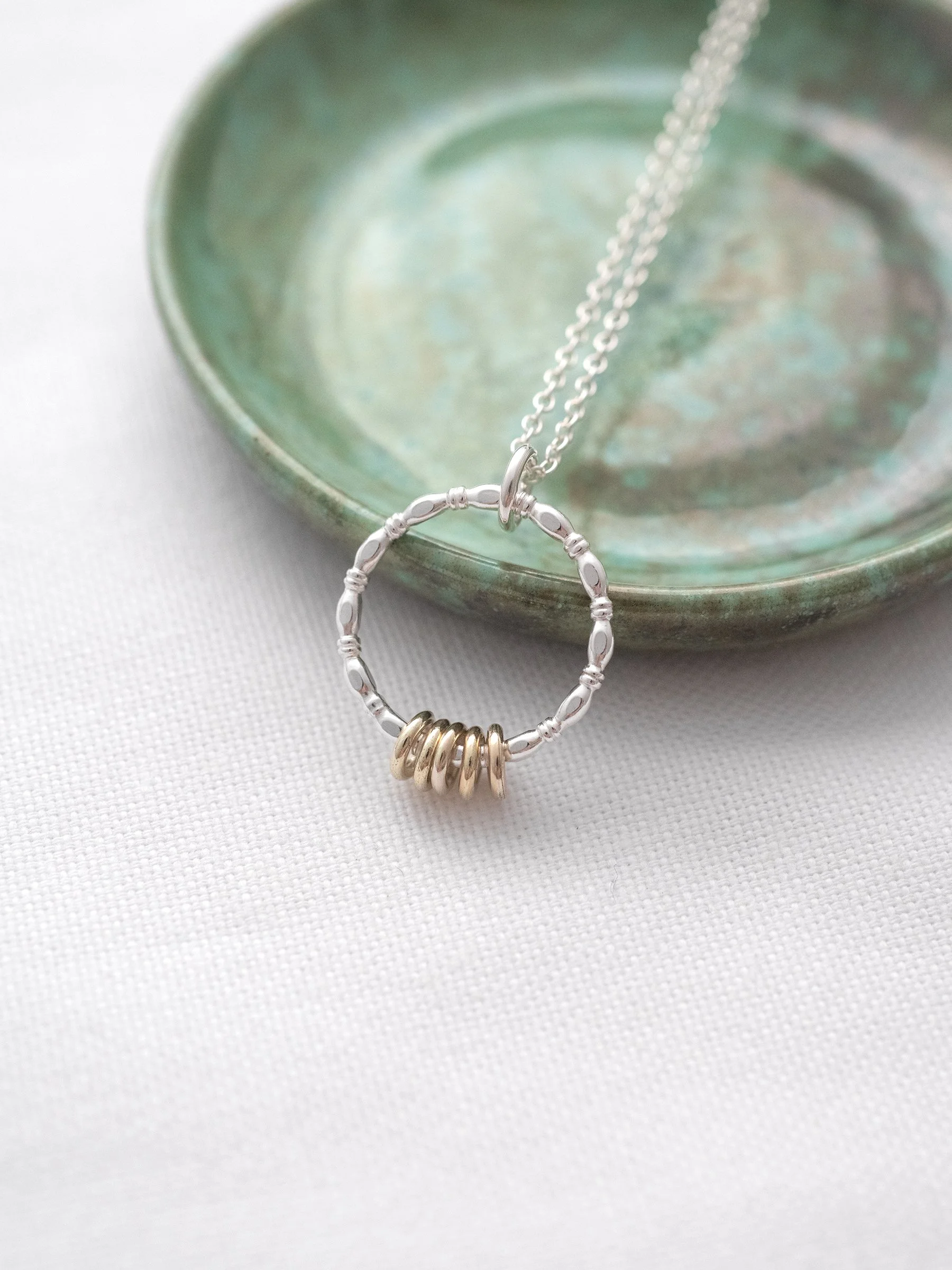 A five ring necklace for a 50th birthday displayed against a green jewellery dish.