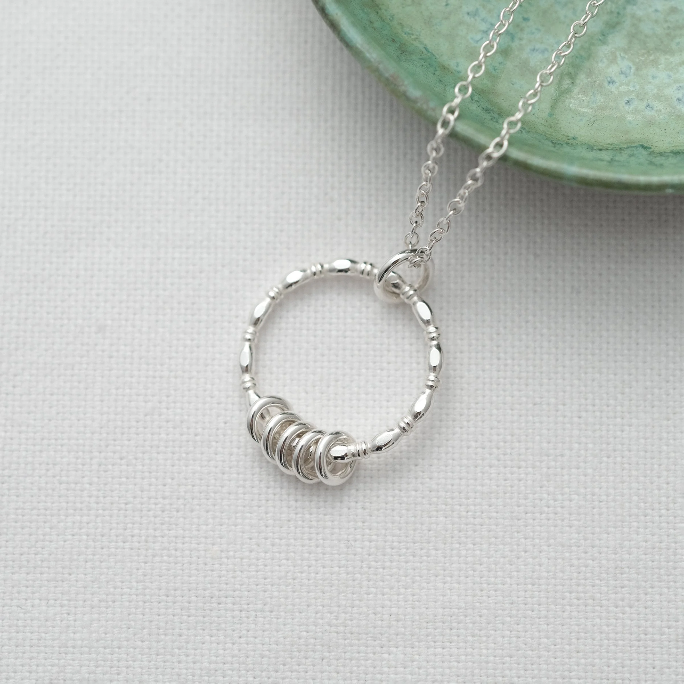 A unique sterling silver 5 ring necklace displayed over white material.