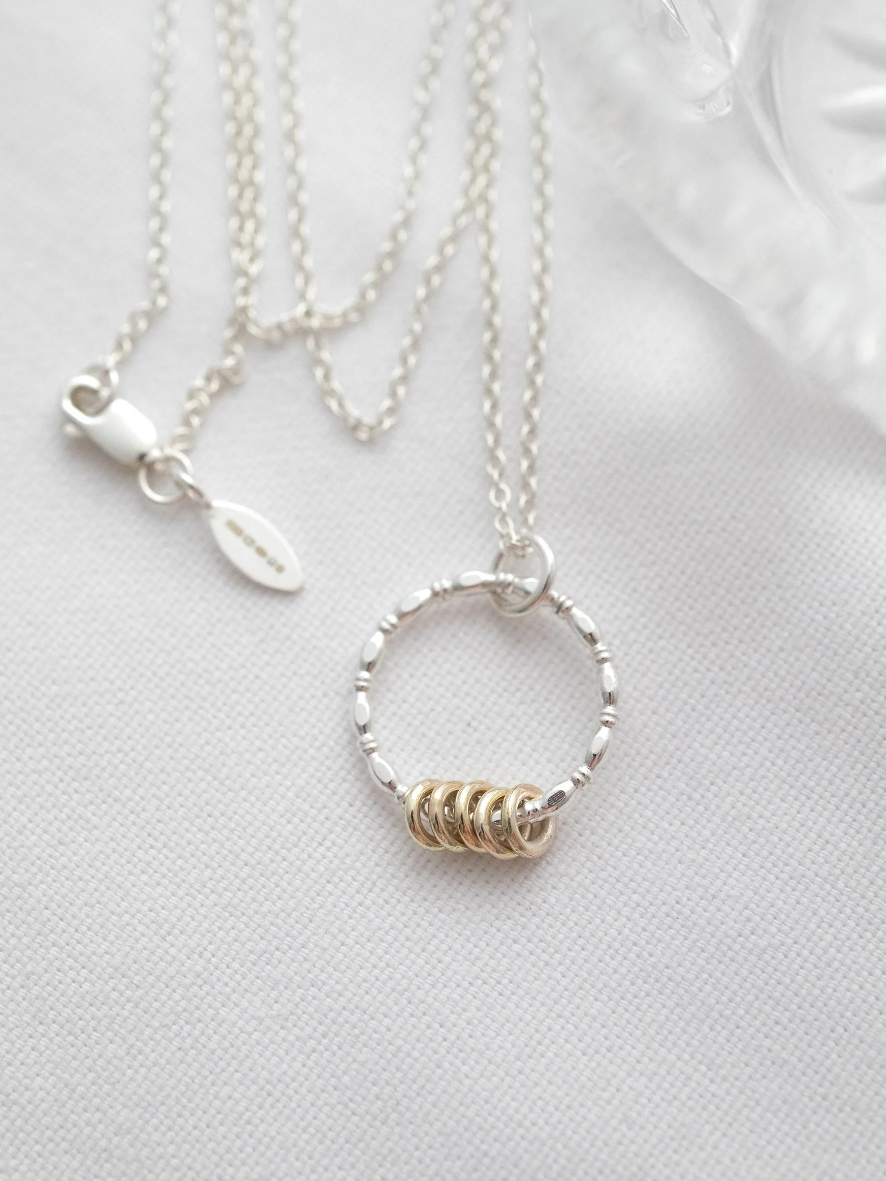 A gold and silver 5 ring necklace on white material showing the sterling silver chain with a hallmark tag.