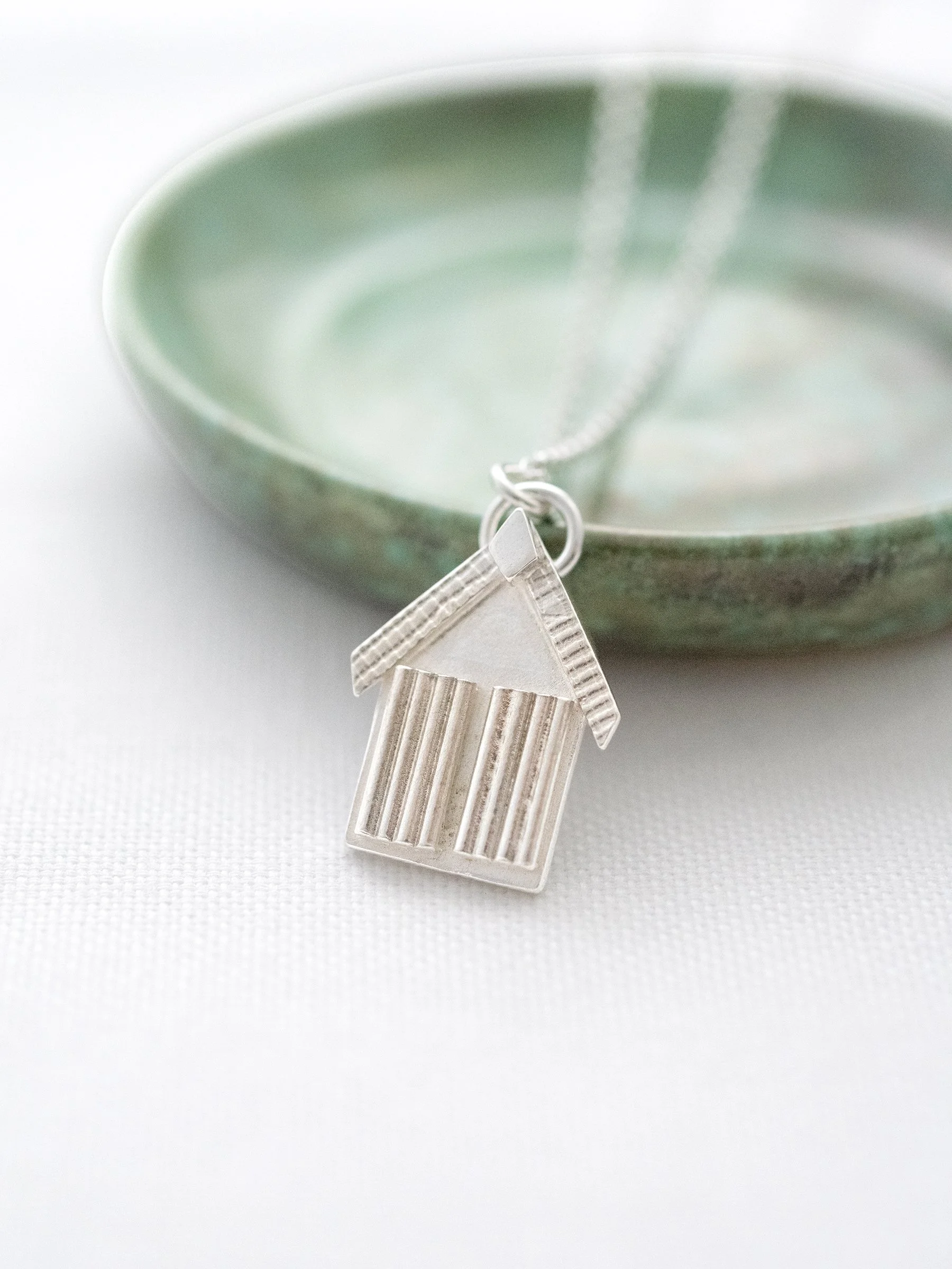 A sterling silver beach hut displayed next to a green jewellery dish.
