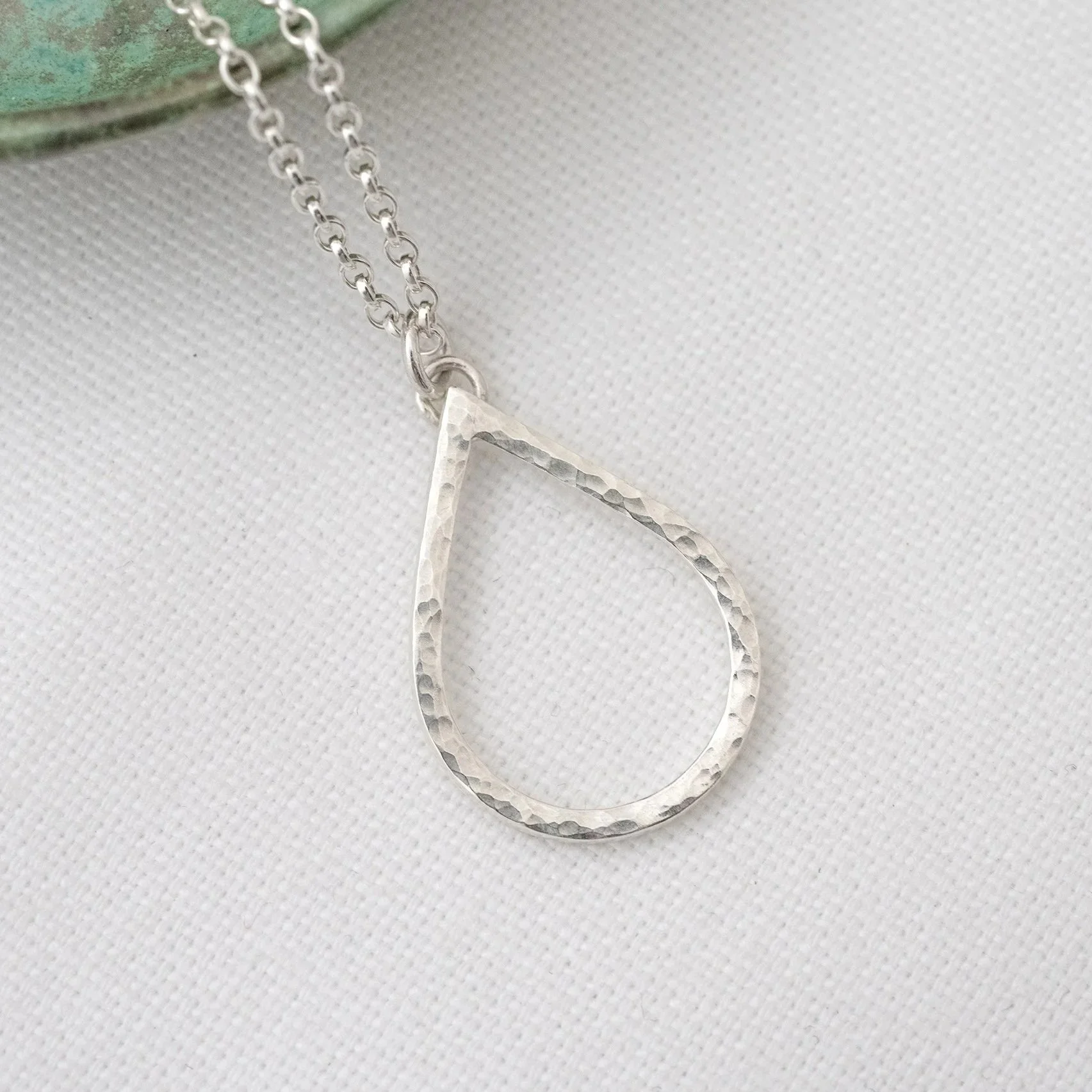 A close up of a sterling silver hammered teardrop shaped necklace.