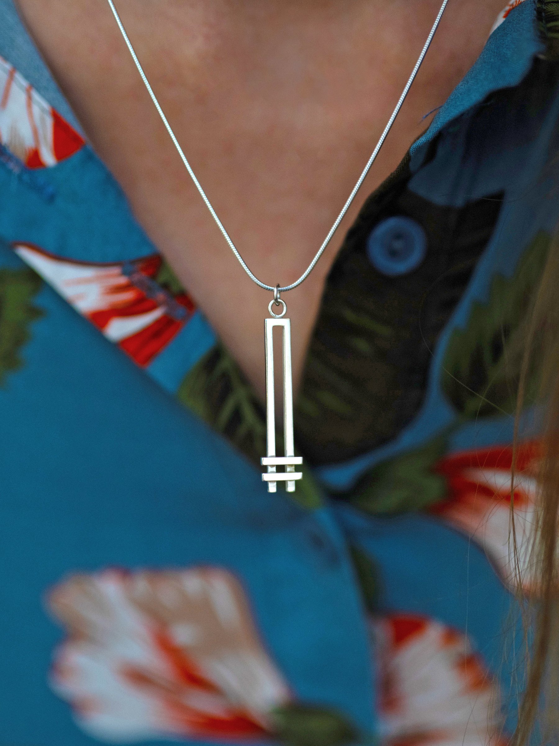 A close up of a person wearing a silver Art Deco style necklace against a blue and red dress.