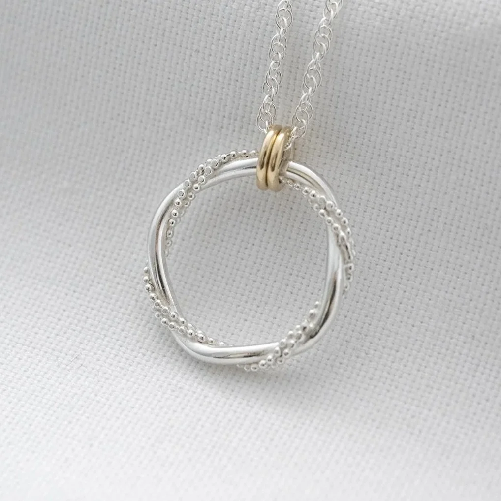 A unique sterling silver necklace with 9ct gold rings displayed over white material.