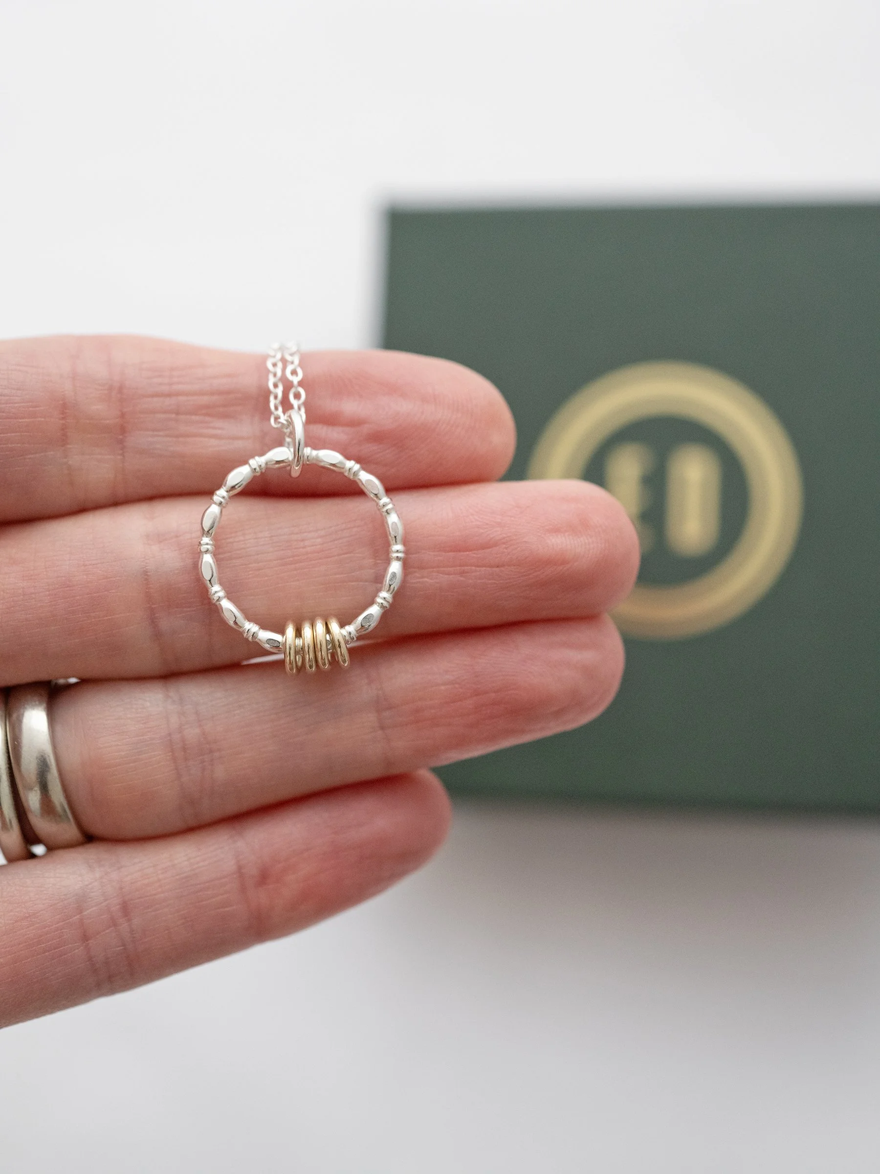 A gold and silver 40th birthday necklace displayed over a persons hand with the presentation box in the background.