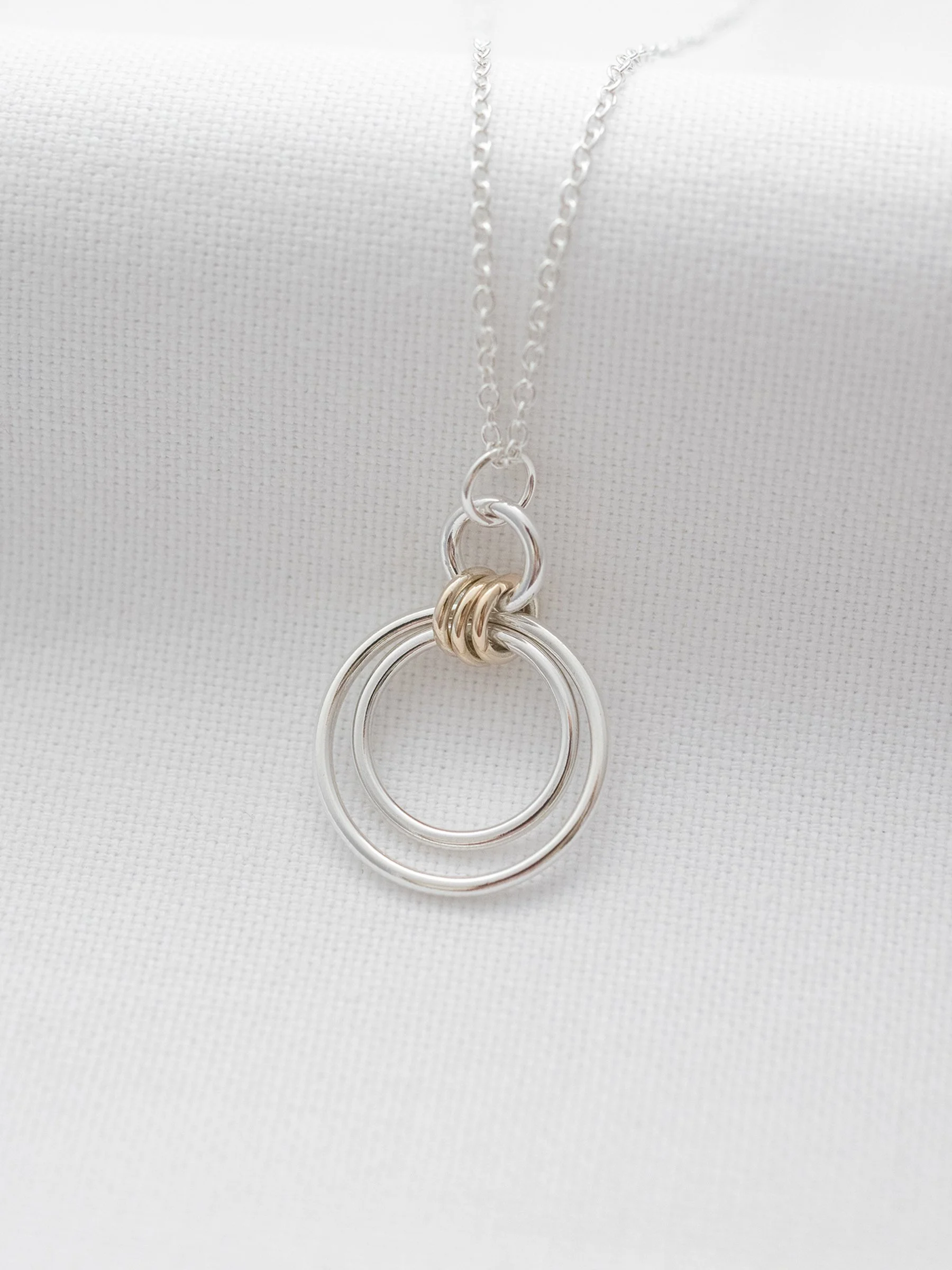 A gold and silver interlinked three ring necklace displayed over white material.