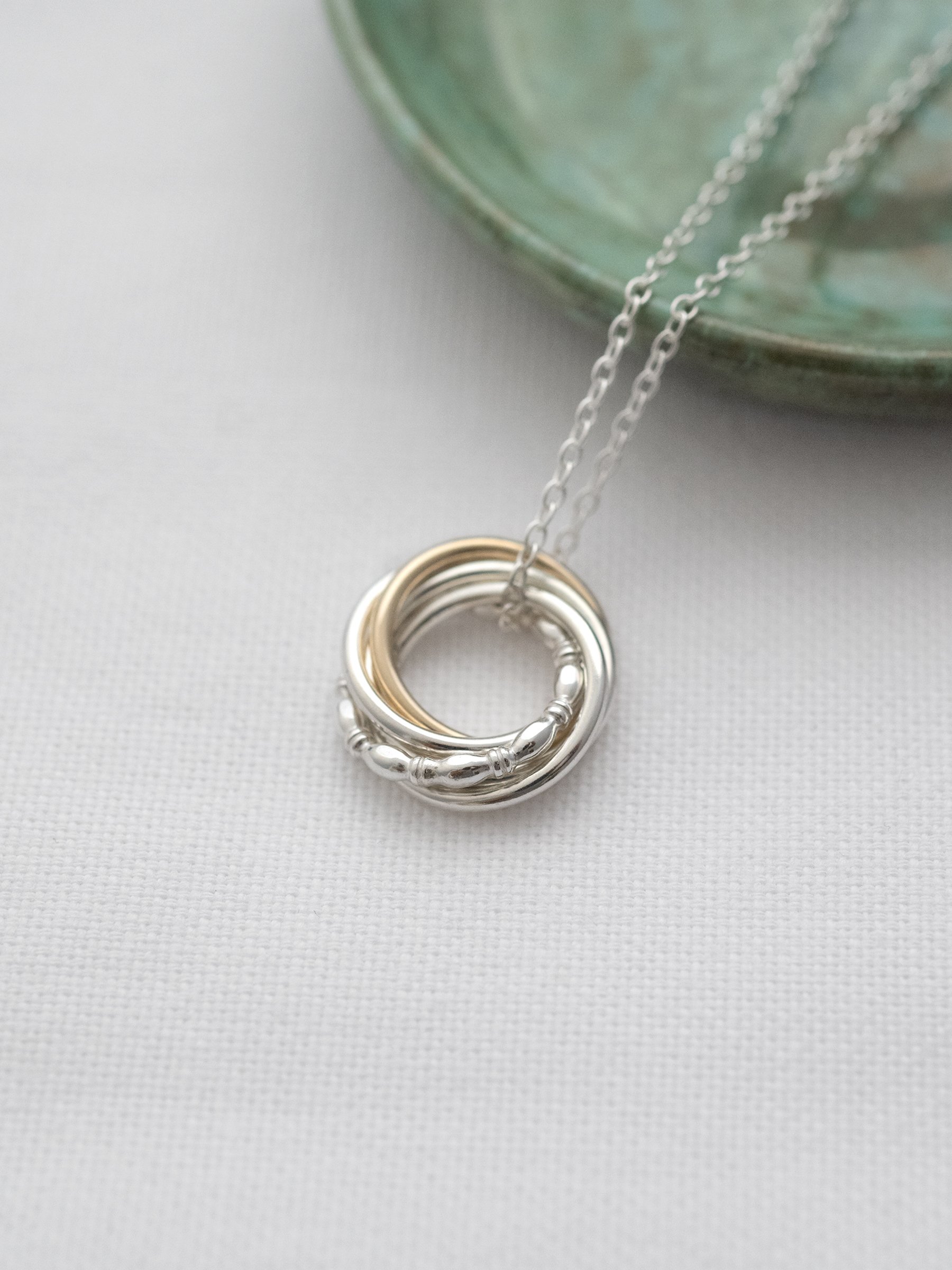 Handmade gold and silver necklace for 50th birthday displayed on white material with a green jewellery dish in the background.