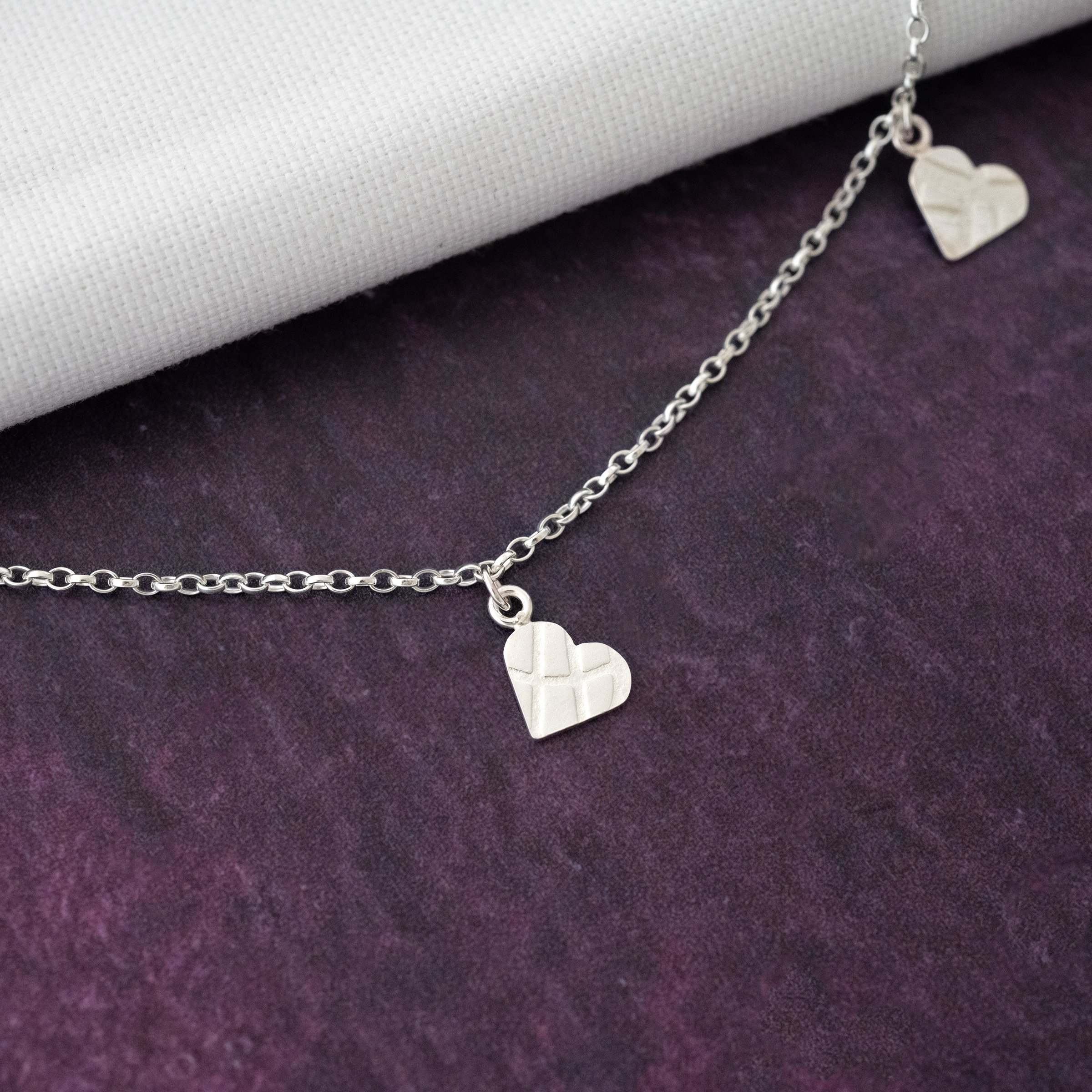 A close up of a heart charm necklace against a purple background.