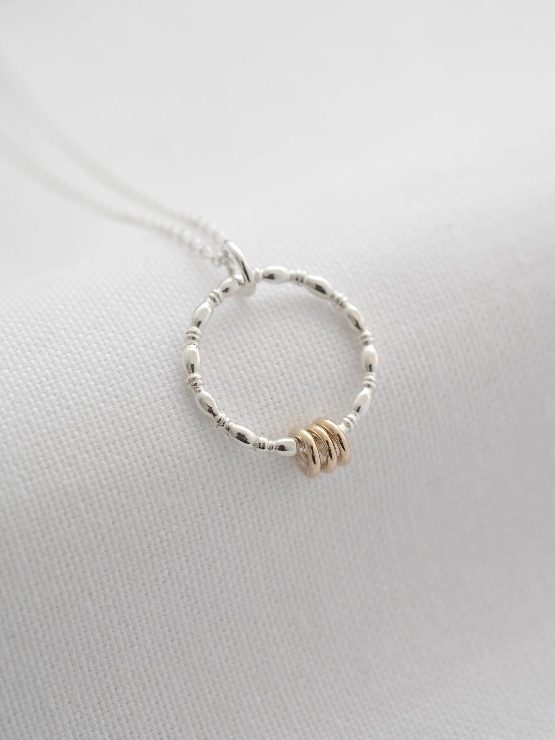 A gold and silver 3 ring necklace displayed over white material.