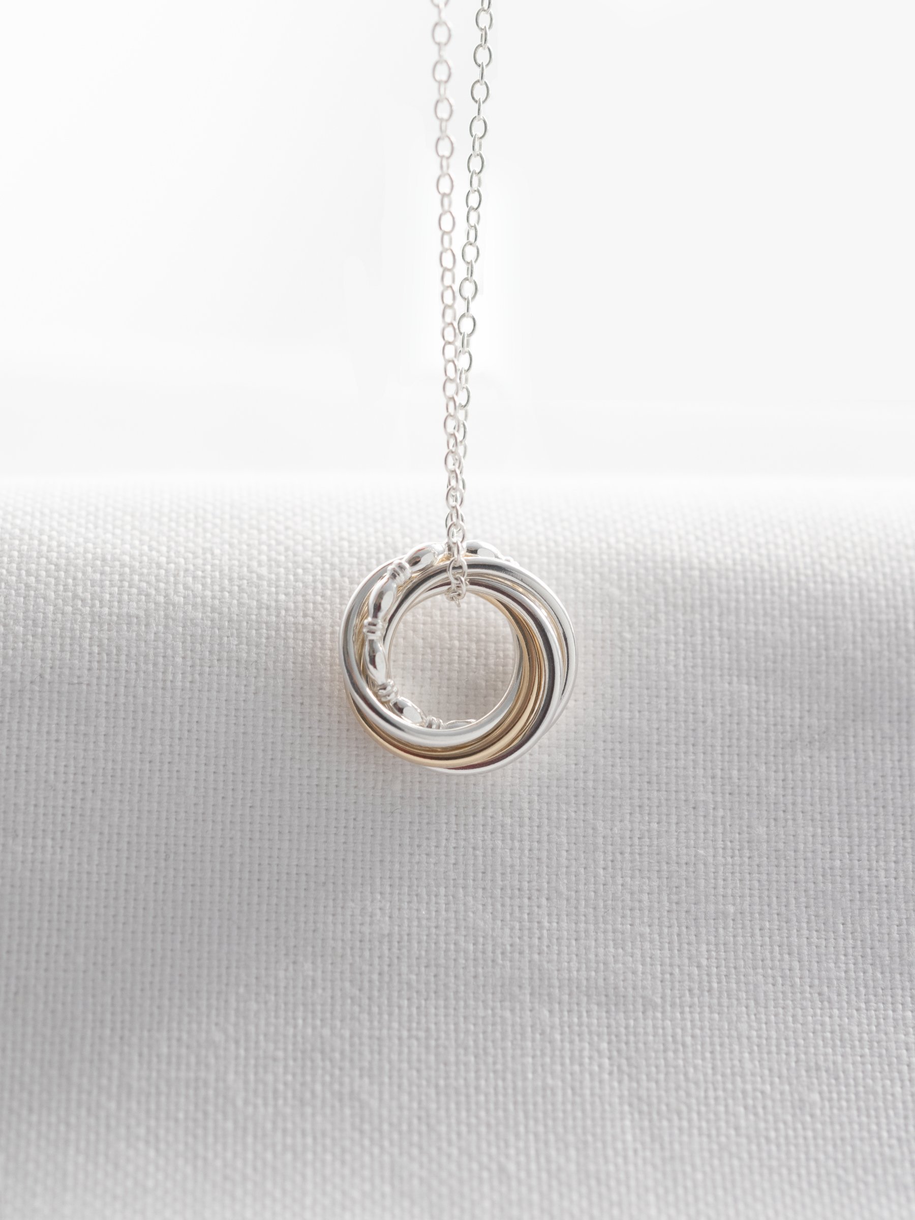 A five ring gold and silver necklace for a 50th birthday hanging over white material.