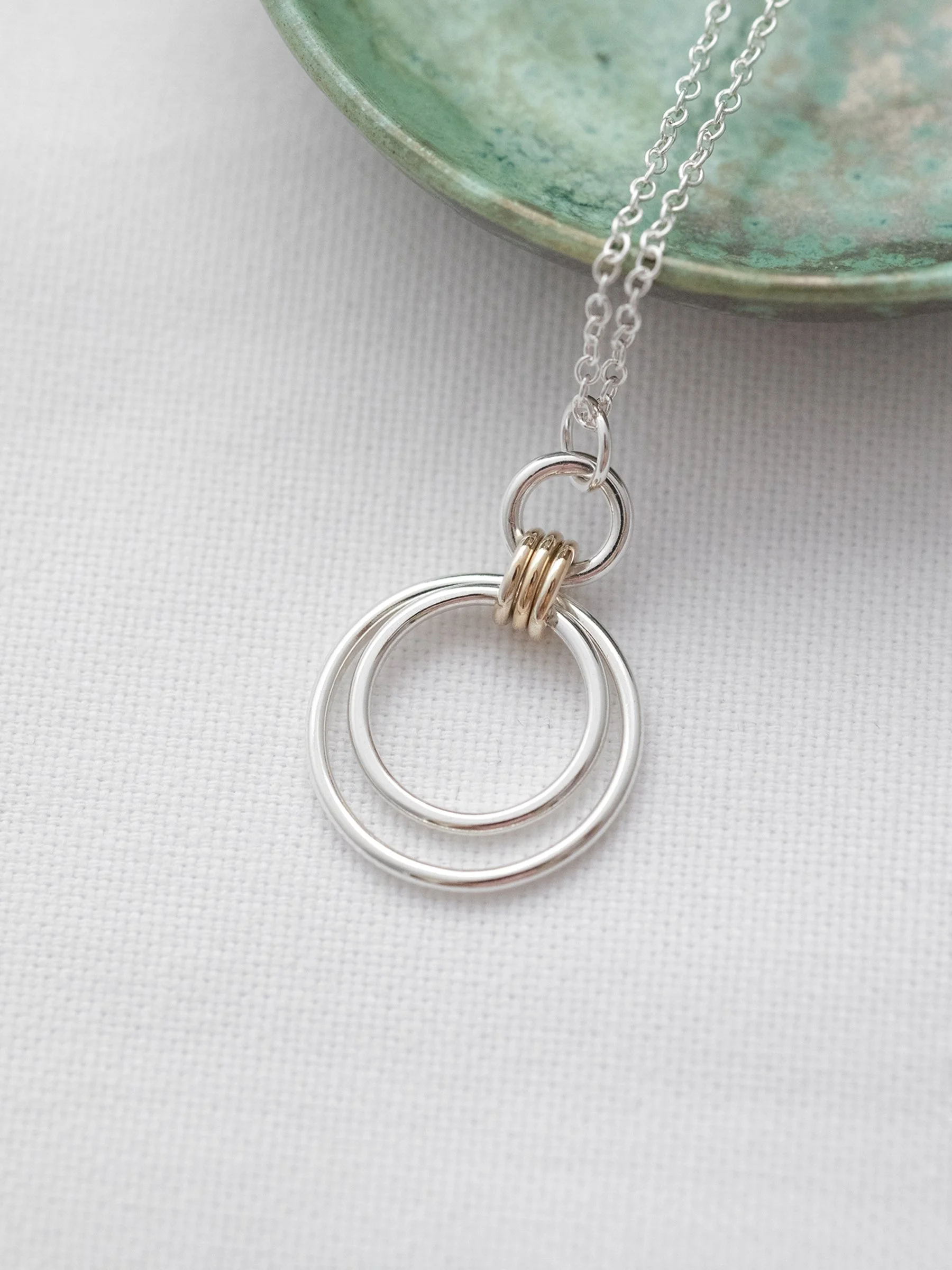 A close up of a three Ring gold and silver Circle Necklace with a green jewellery dish in the background.