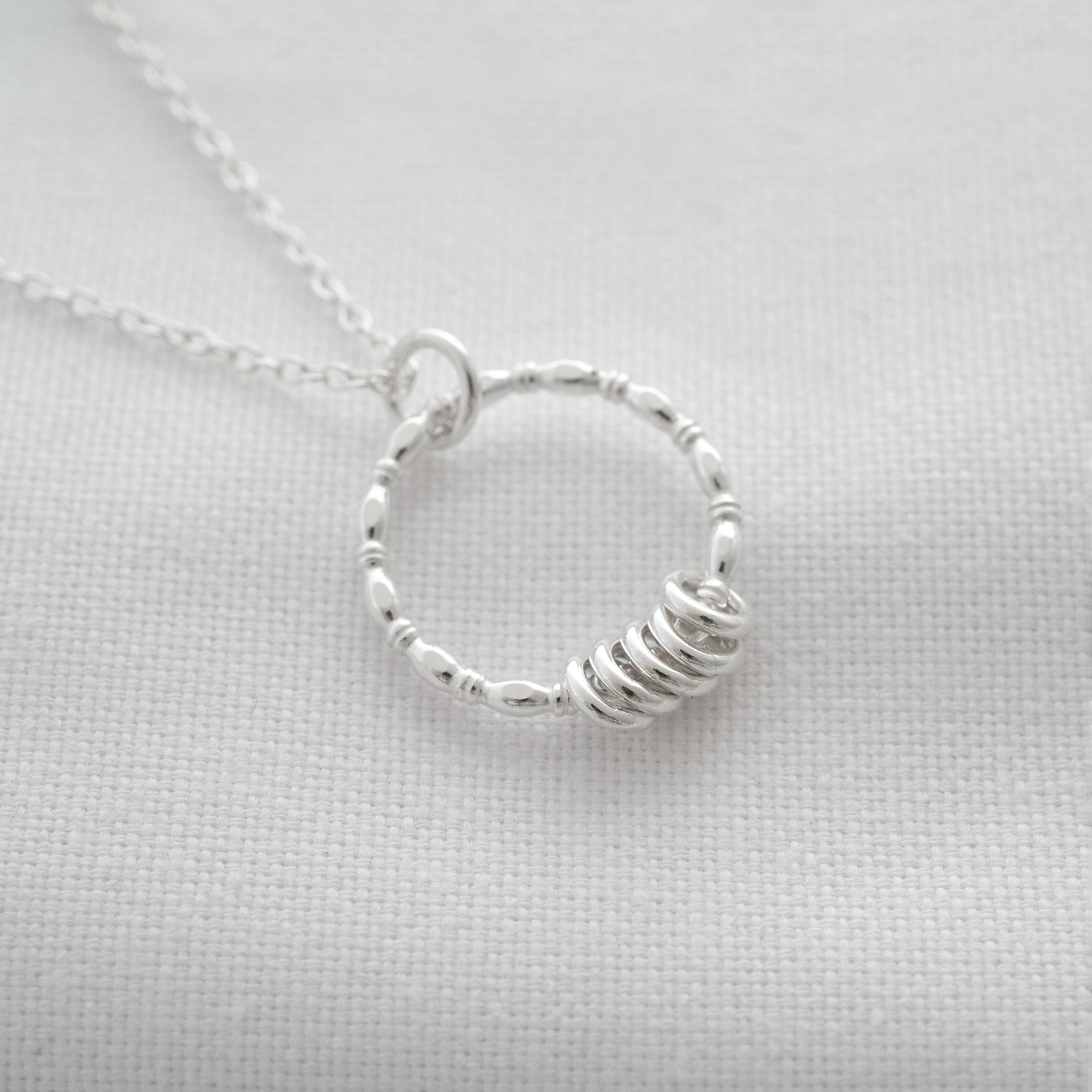 A sterling silver five ring necklace displayed on white material.