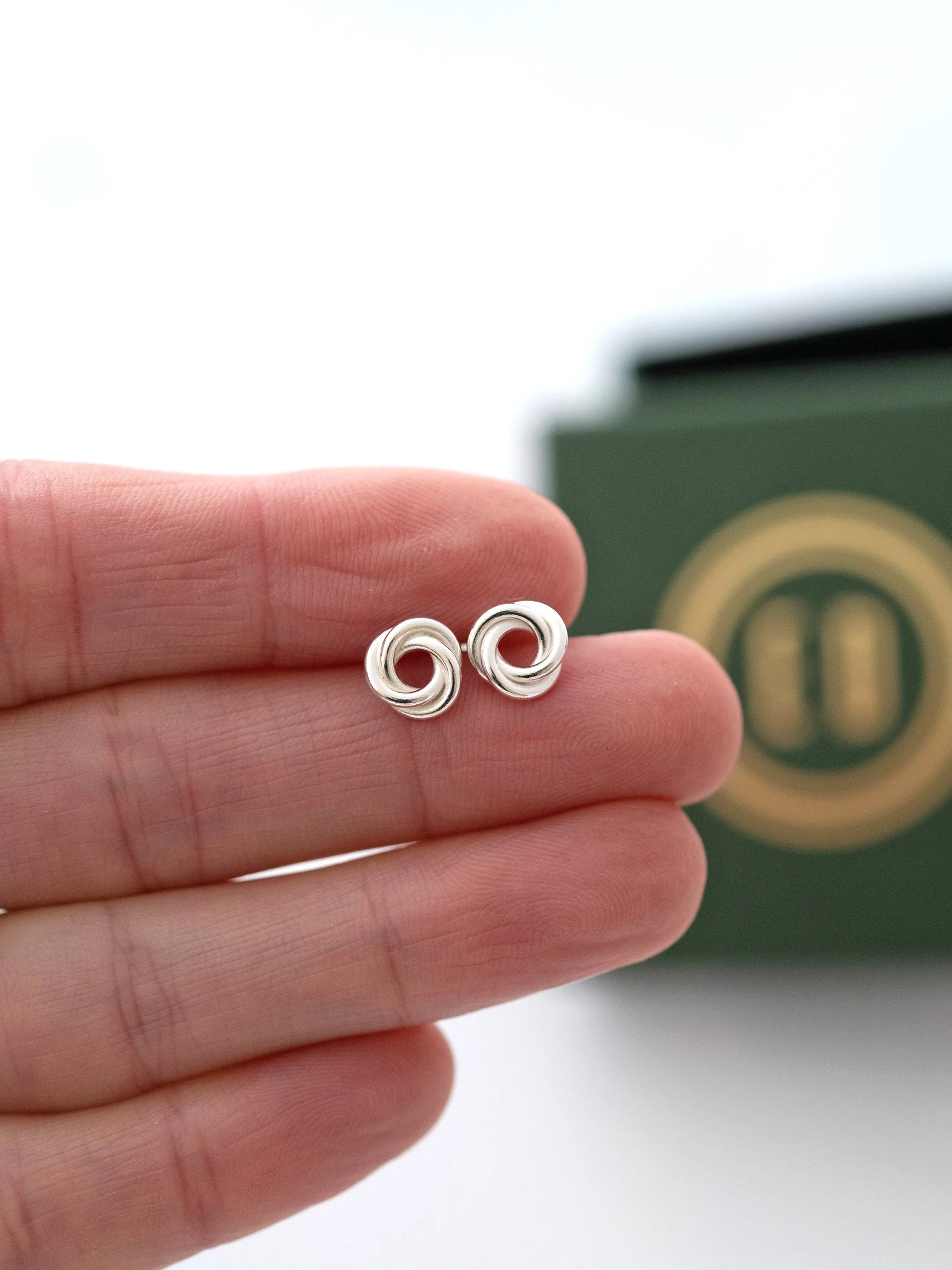 A pair of Russian ring stud earrings displayed on a persons hand with the presentation box in the background.