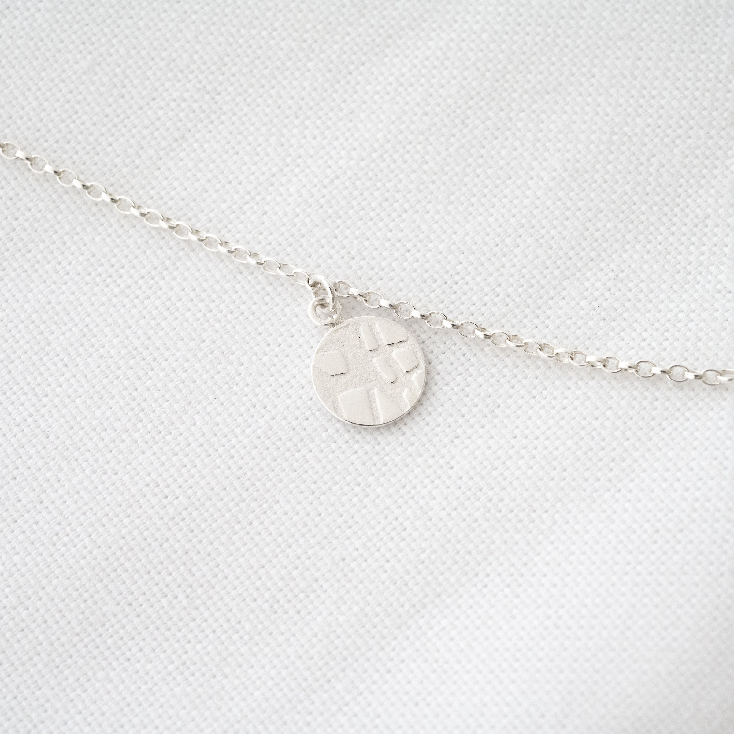 A close up of a silver circle charm necklace displayed on white material.