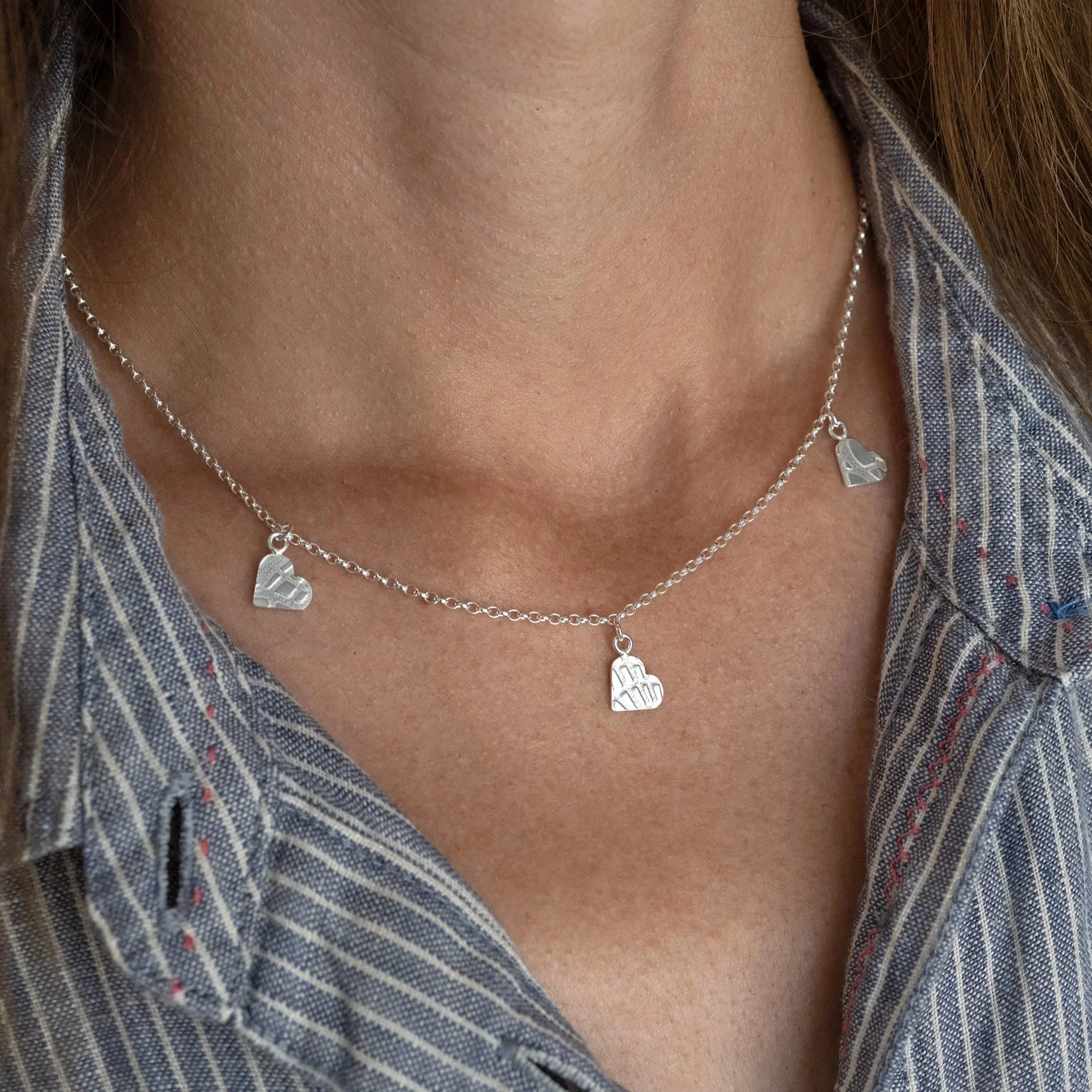 A close up of a person wearing a sterling silver heart necklace against a blue and white dress.