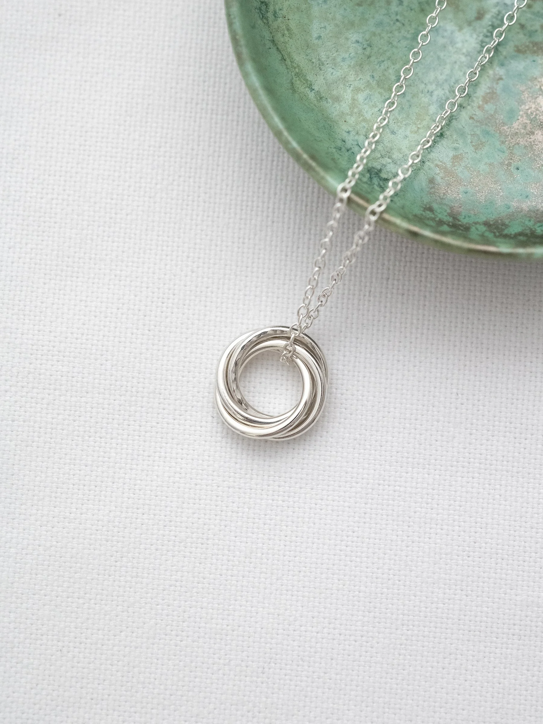 A sterling silver 40th birthday necklace displayed on white material with a green jewellery dish in the background.