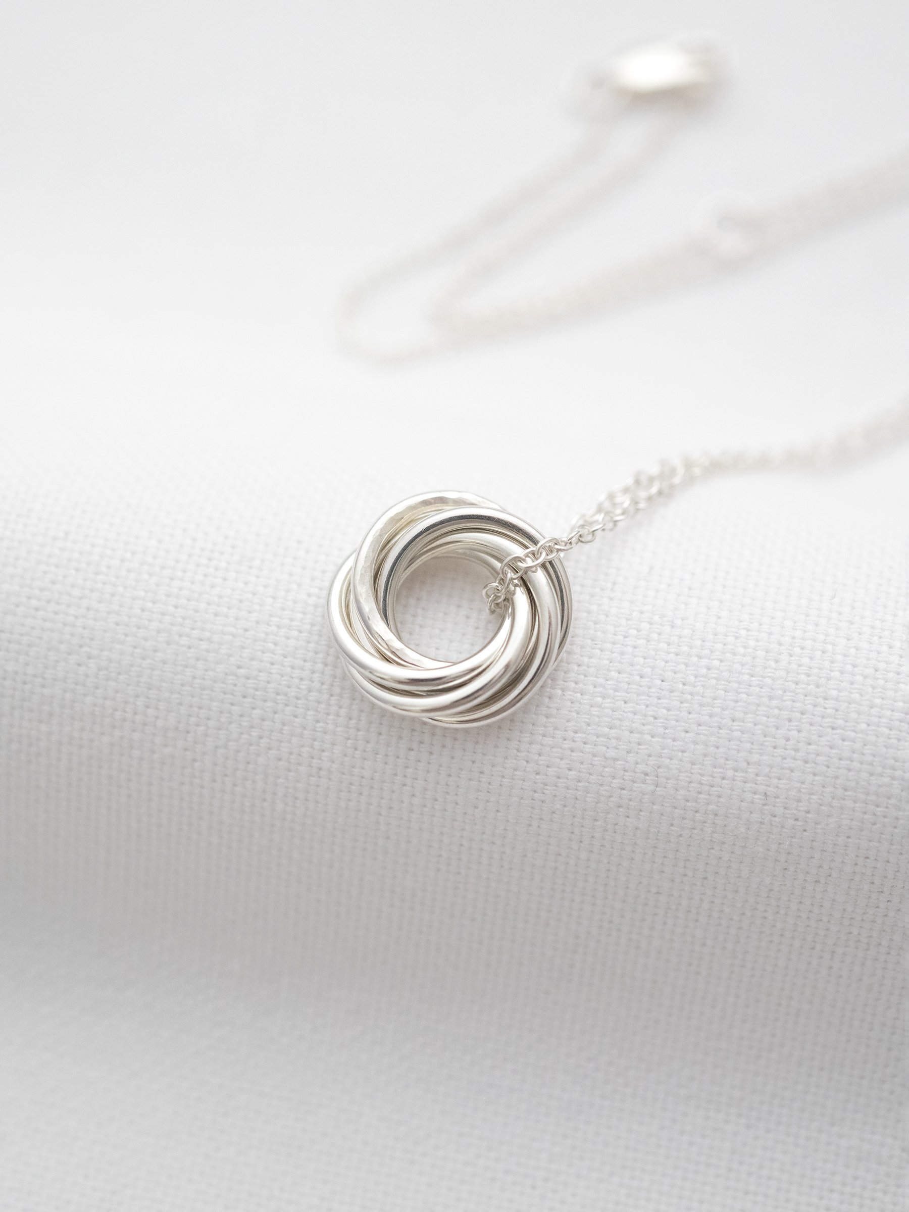 A sterling silver 60th necklace displayed on white material with the chain in the background.