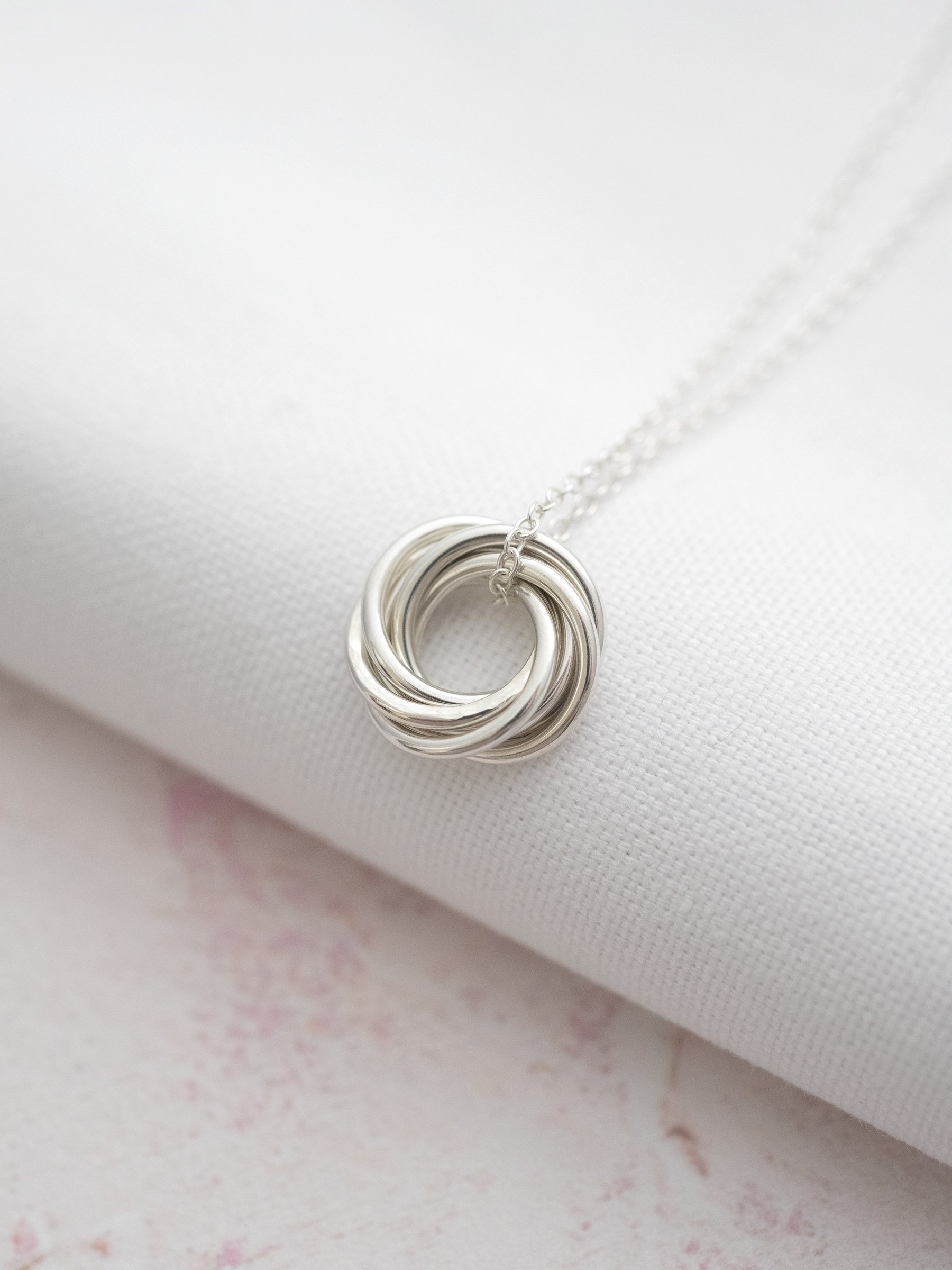 A side view of a 60th necklace displayed on white material against a light pink background.