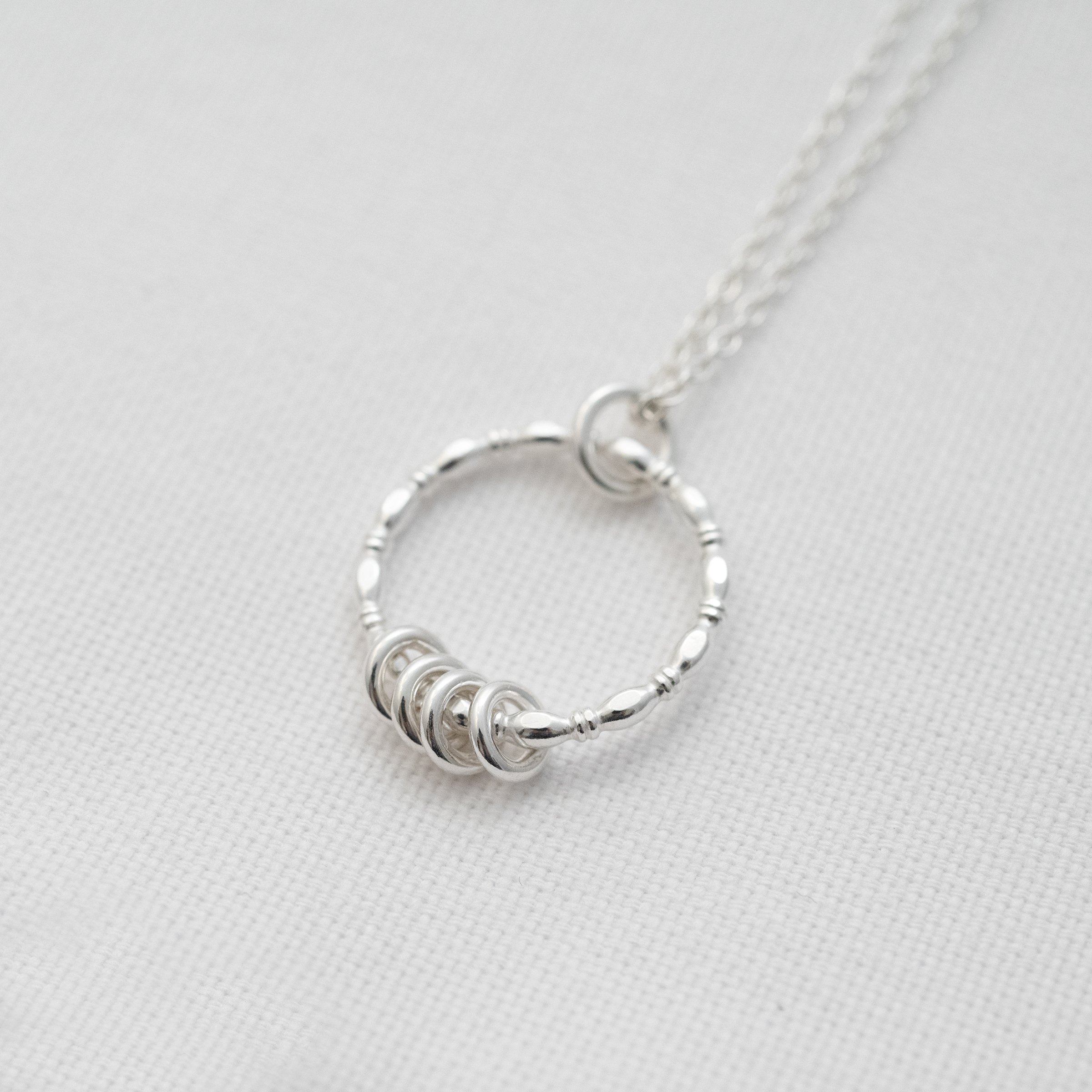 A side view of a silver 40th birthday necklace displayed on white material.