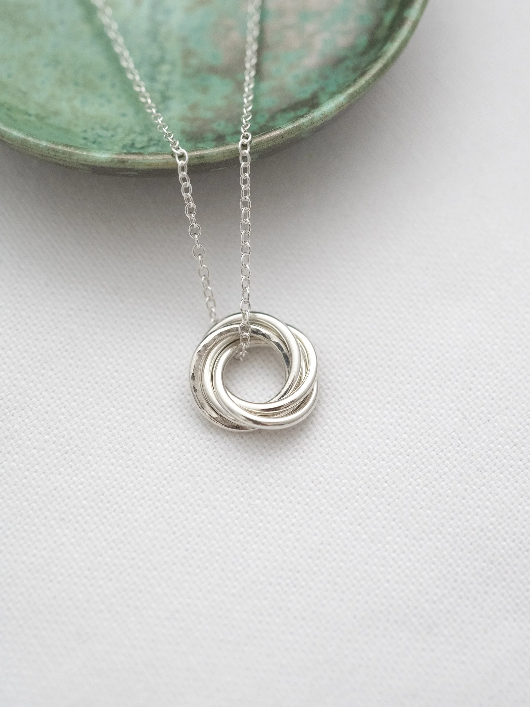 A sterling silver 50th birthday necklace displayed on white material with a green jewellery dish in the background.