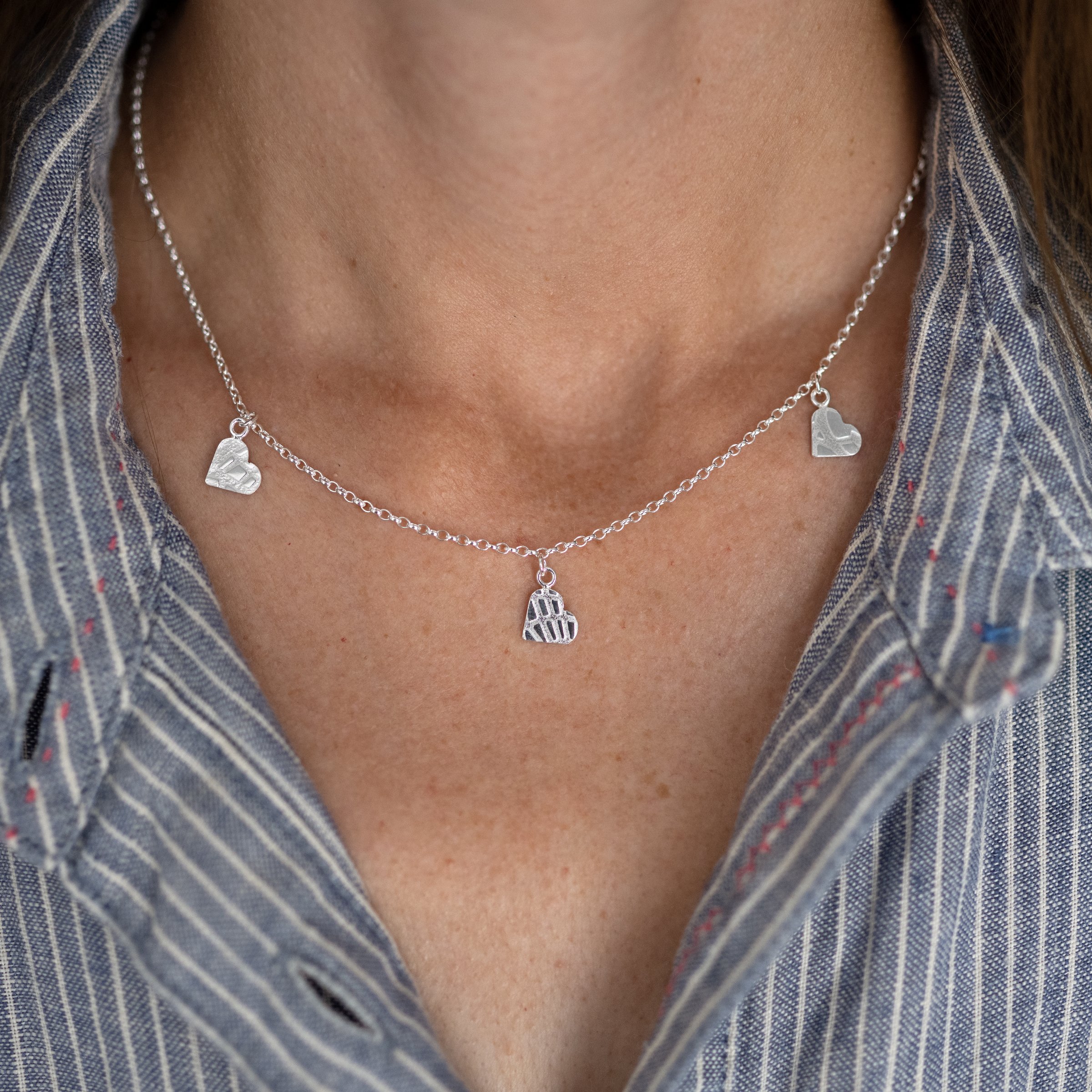 A person wearing a silver three heart charm necklace against a blue and white striped dress.