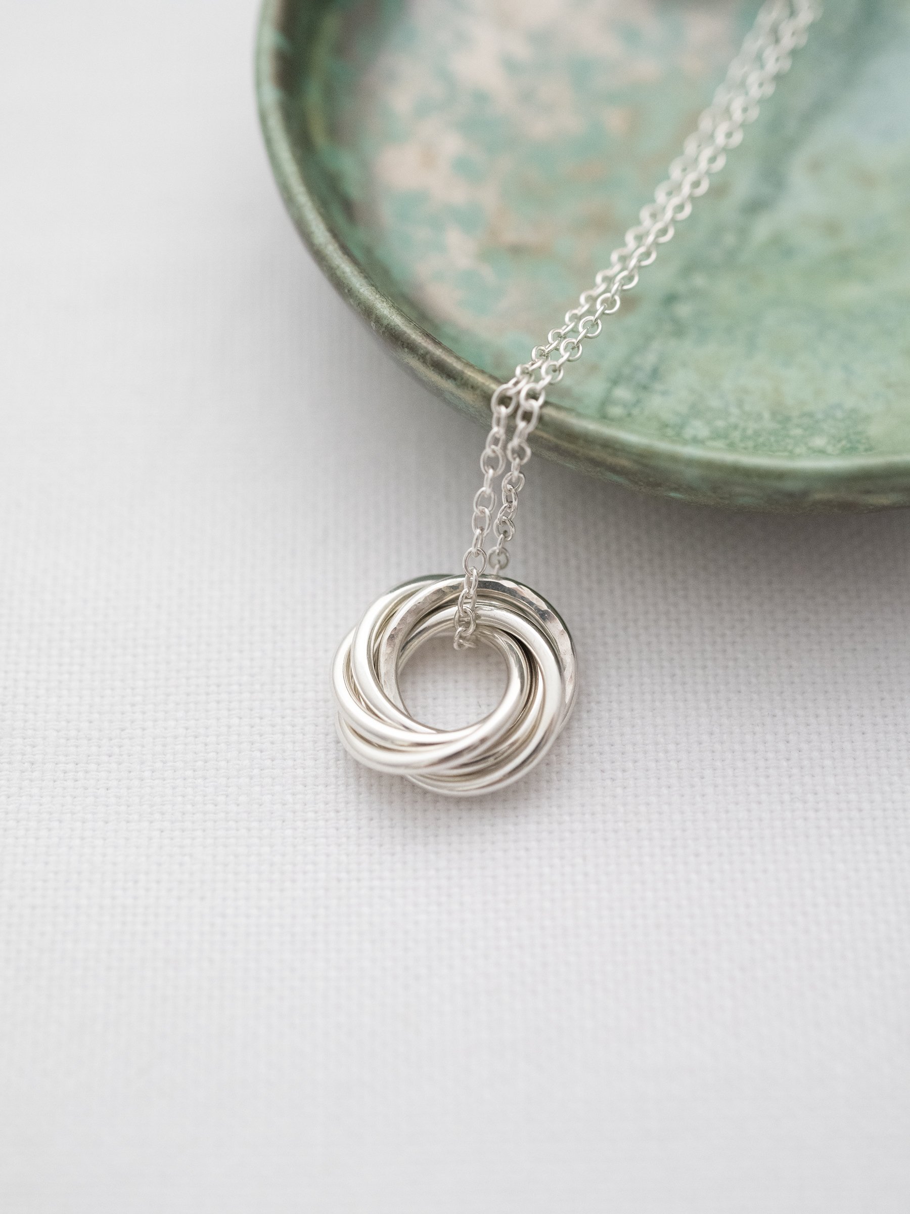 A close up of a silver 60th birthday necklace with a green jewellery dish in the background.