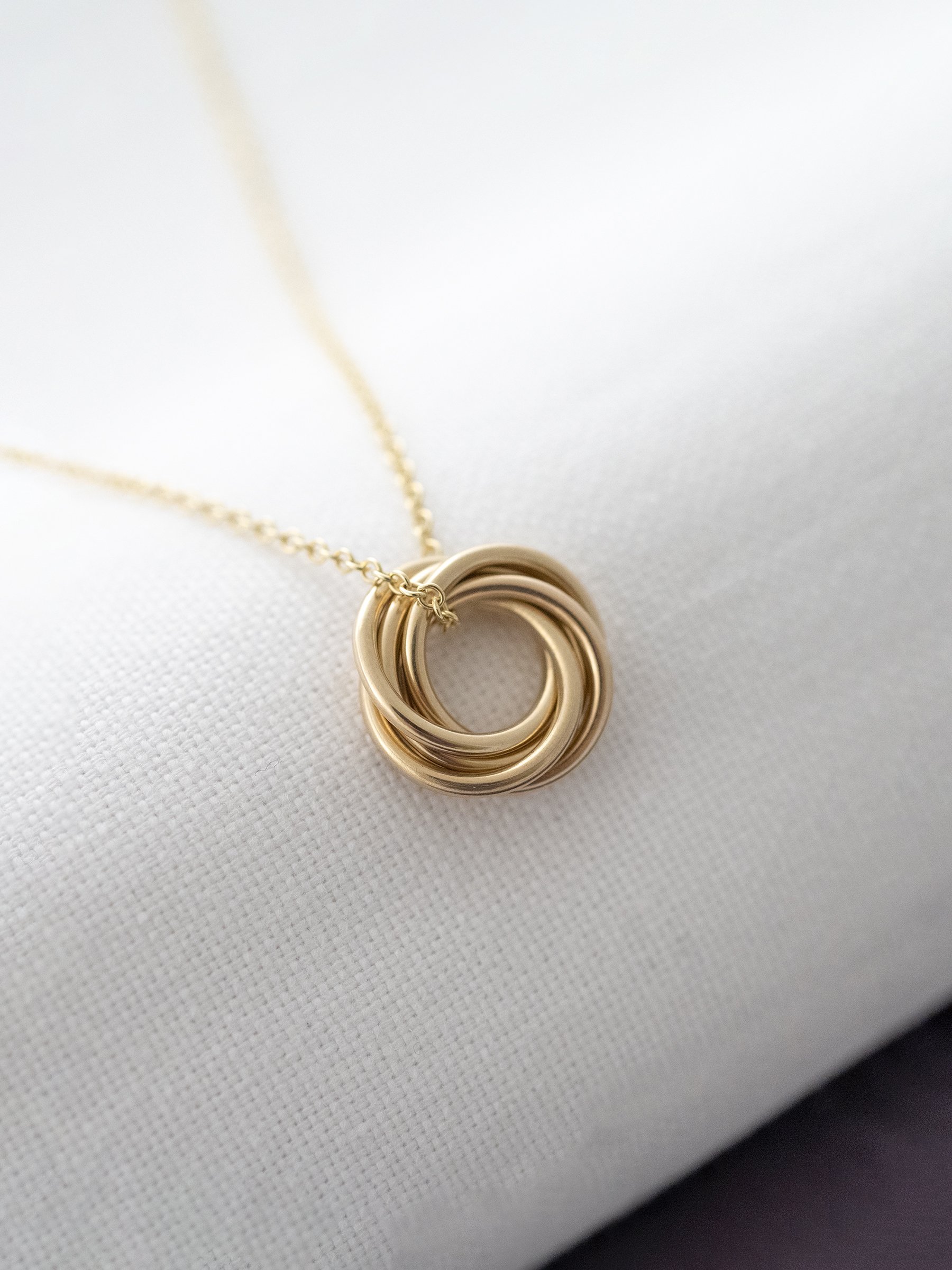 A side view of a 9ct gold five ring necklace displayed over white material.