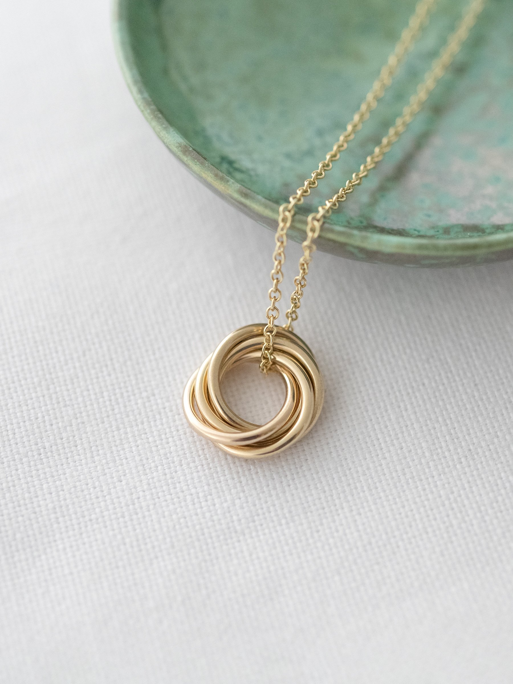 A gold 50th necklace displayed over white material and a green jewellery trinket dish.