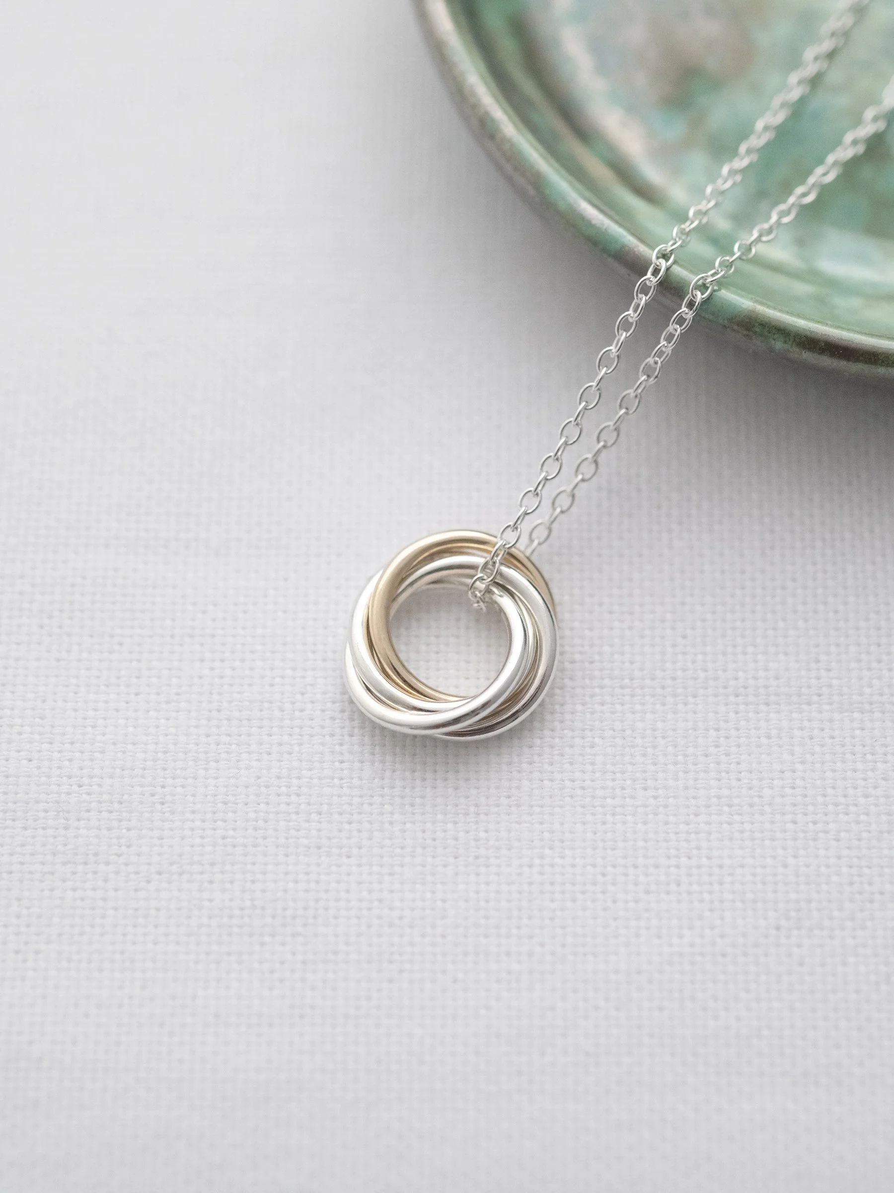 A unique gold and silver necklace for a 40th birthday displayed on white material with a green jewellery dish in the background.