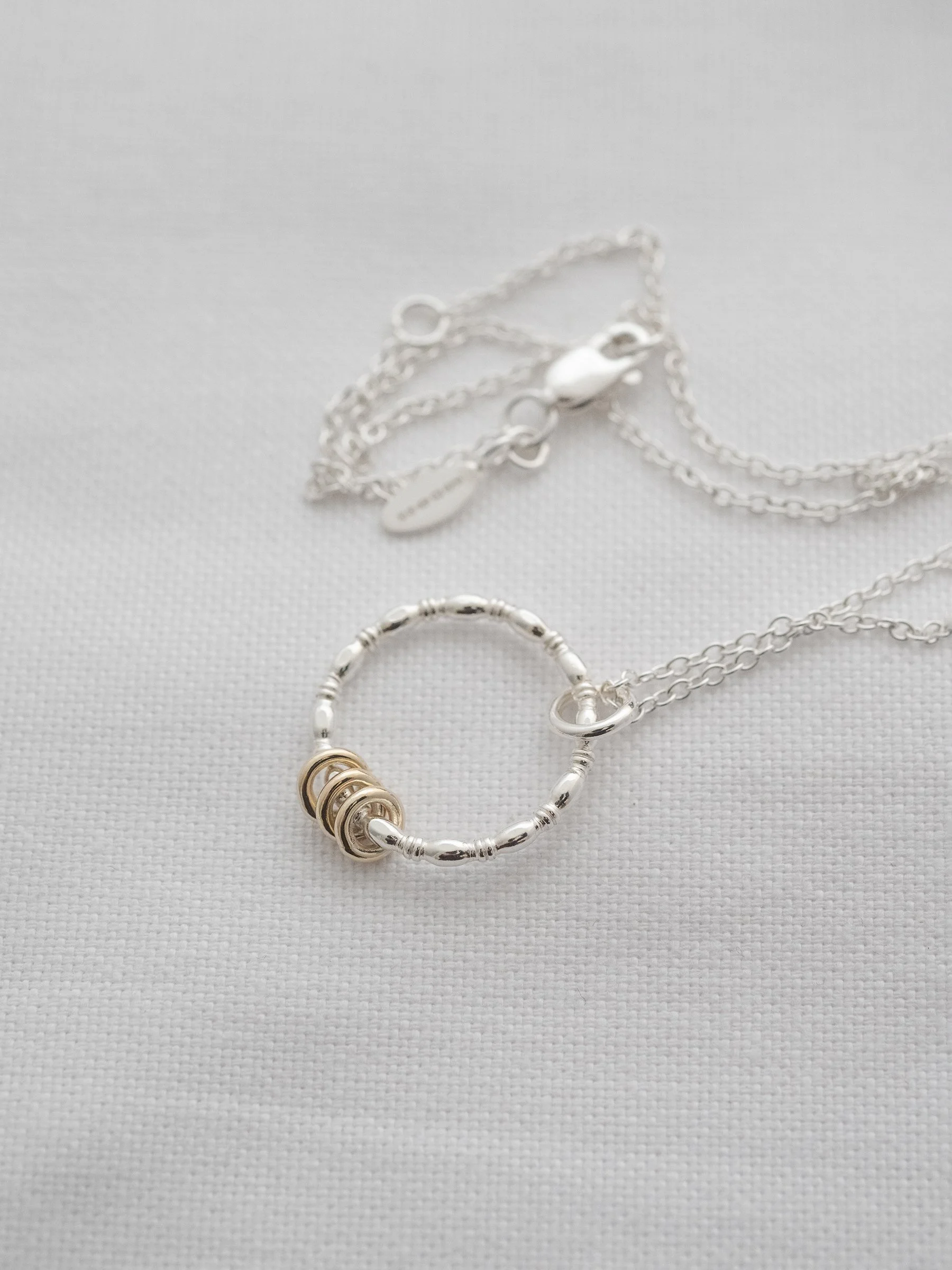 A unique gold and silver 3 ring necklace displayed over white material.
