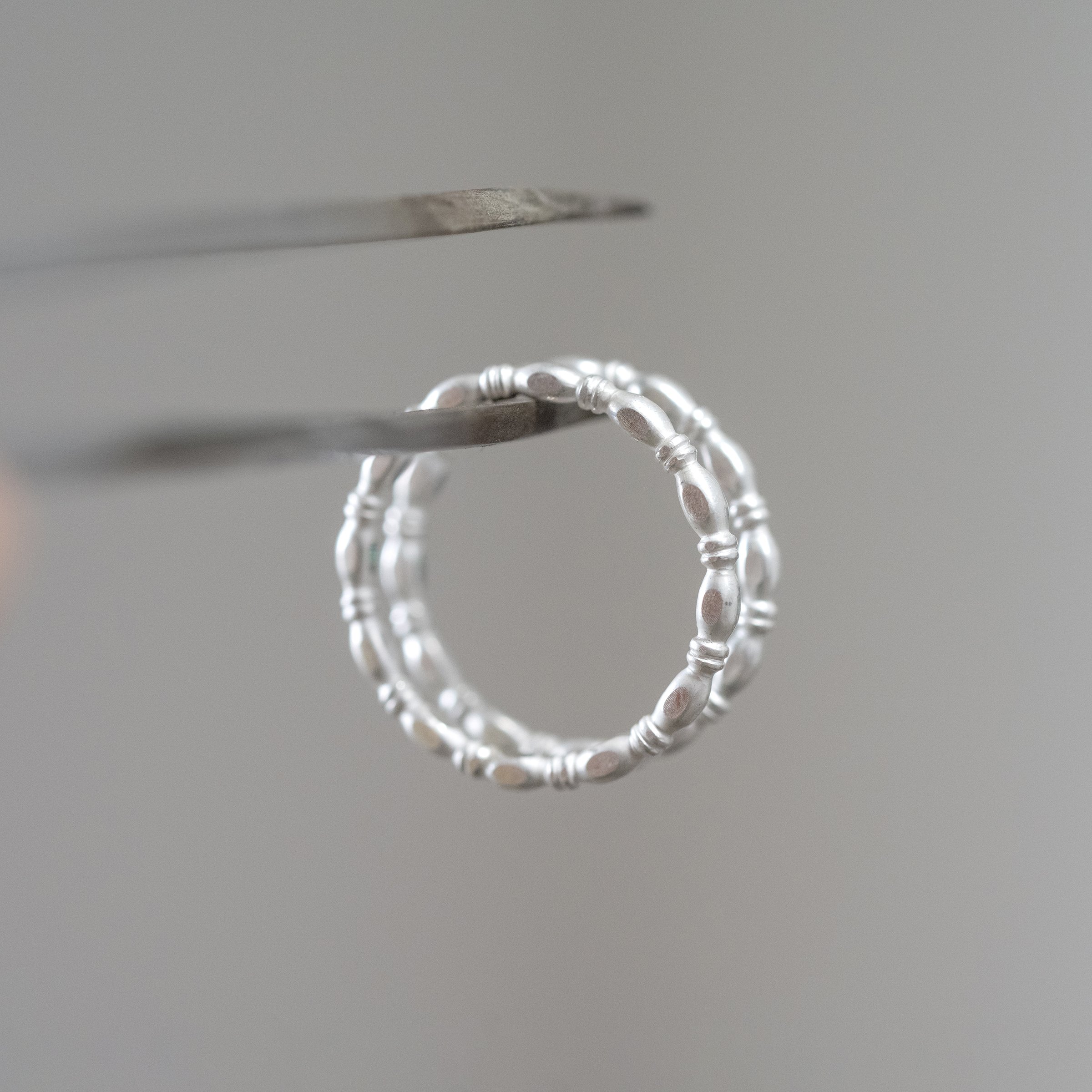 A detailed close up of two decorative silver rings hanging on a pair of tweezers.