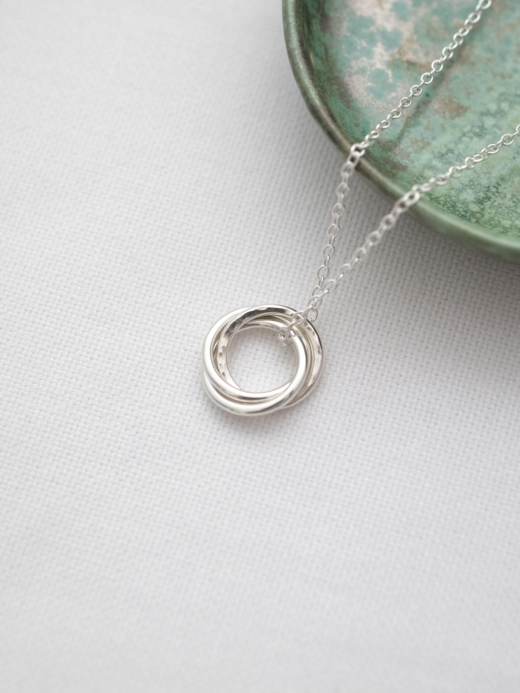 A sterling silver 3 ring necklace for a 30th birthday displayed on white material with a green jewellery dish in the background.