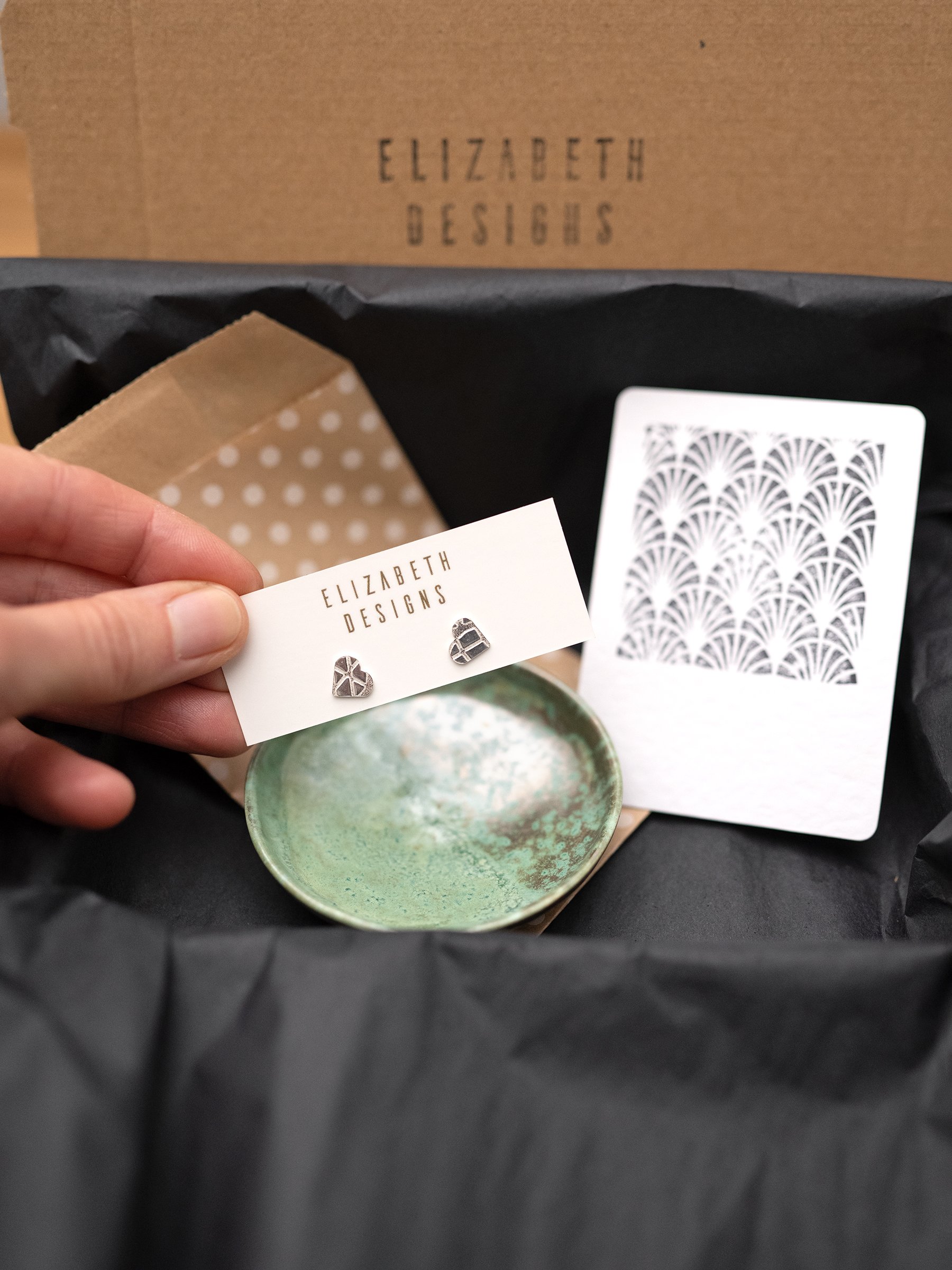 A pair of silver heart earrings and a handmade green jewellery dish presented as a gift package with a gift card.