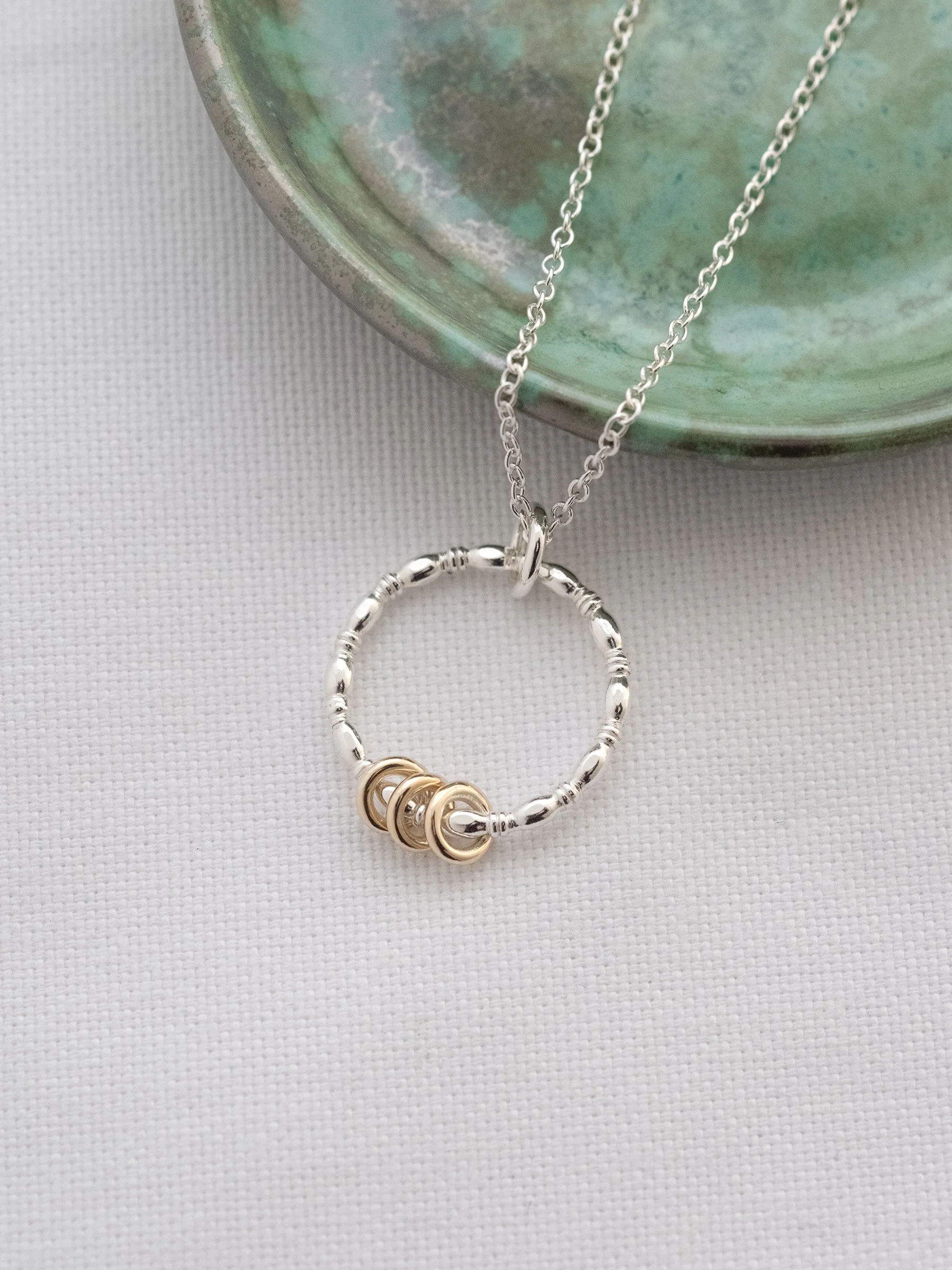 A 30th gold and silver birthday ring necklace displayed on white material with a green jewellery dish in the background.