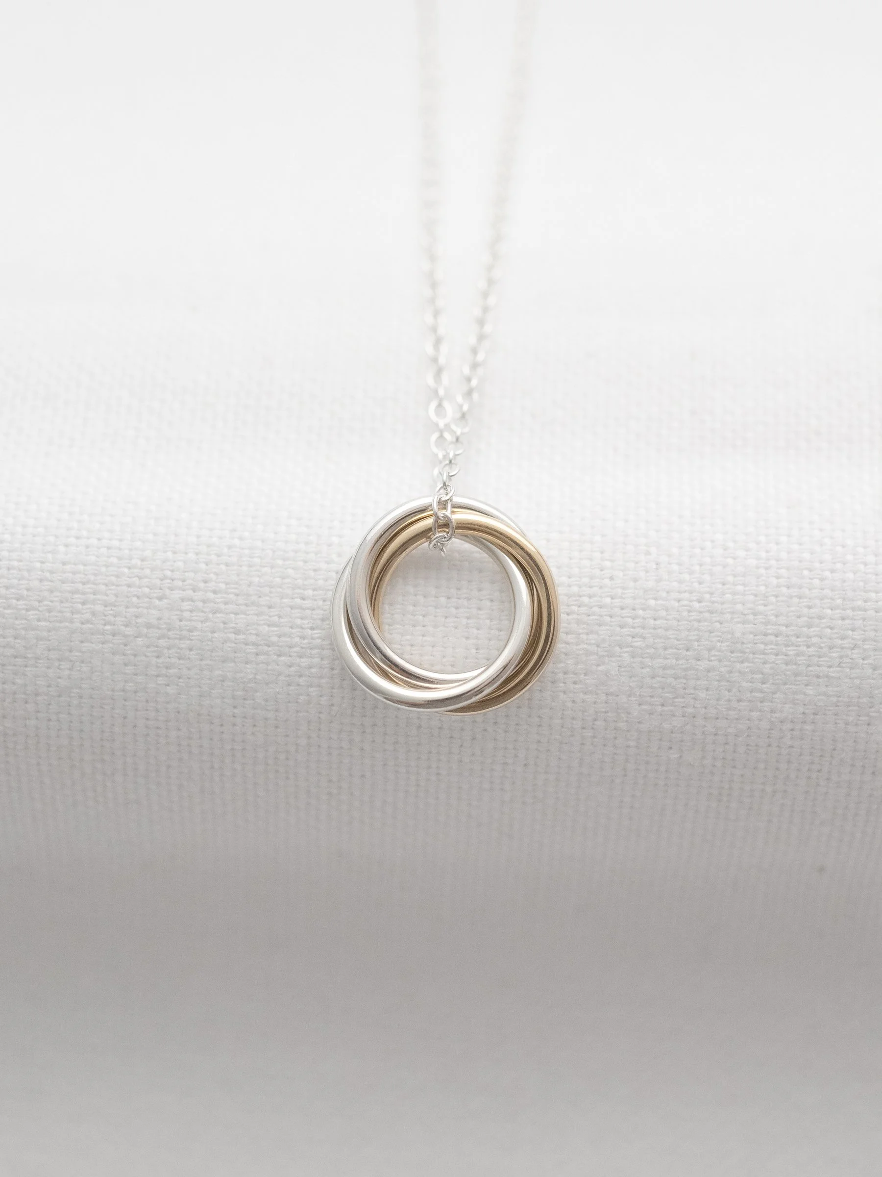 A handmade 3 ring necklace displayed on white material.