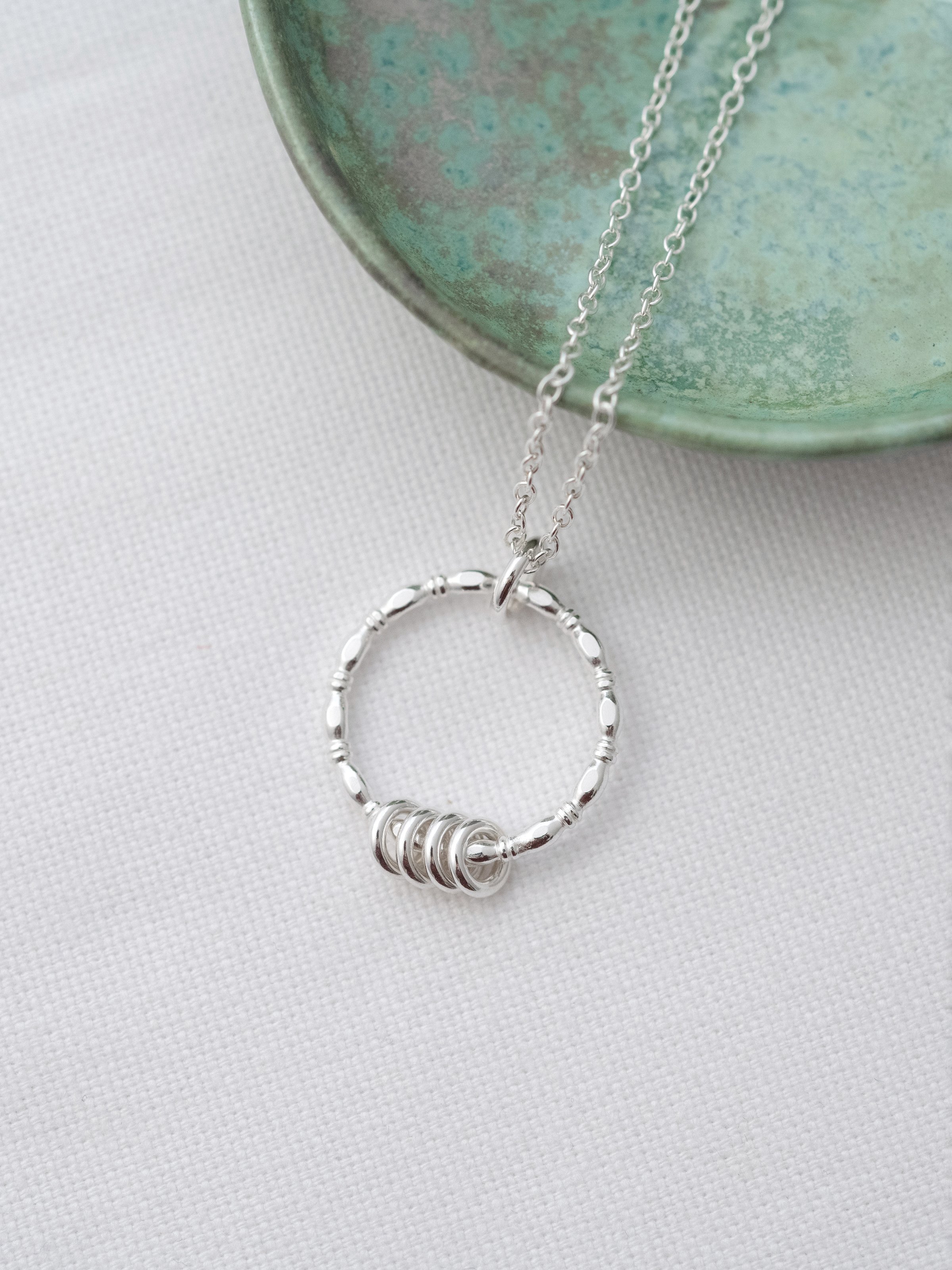 A sterling silver 40th birthday necklace displayed on white material and a turquoise jewellery dish in the background.