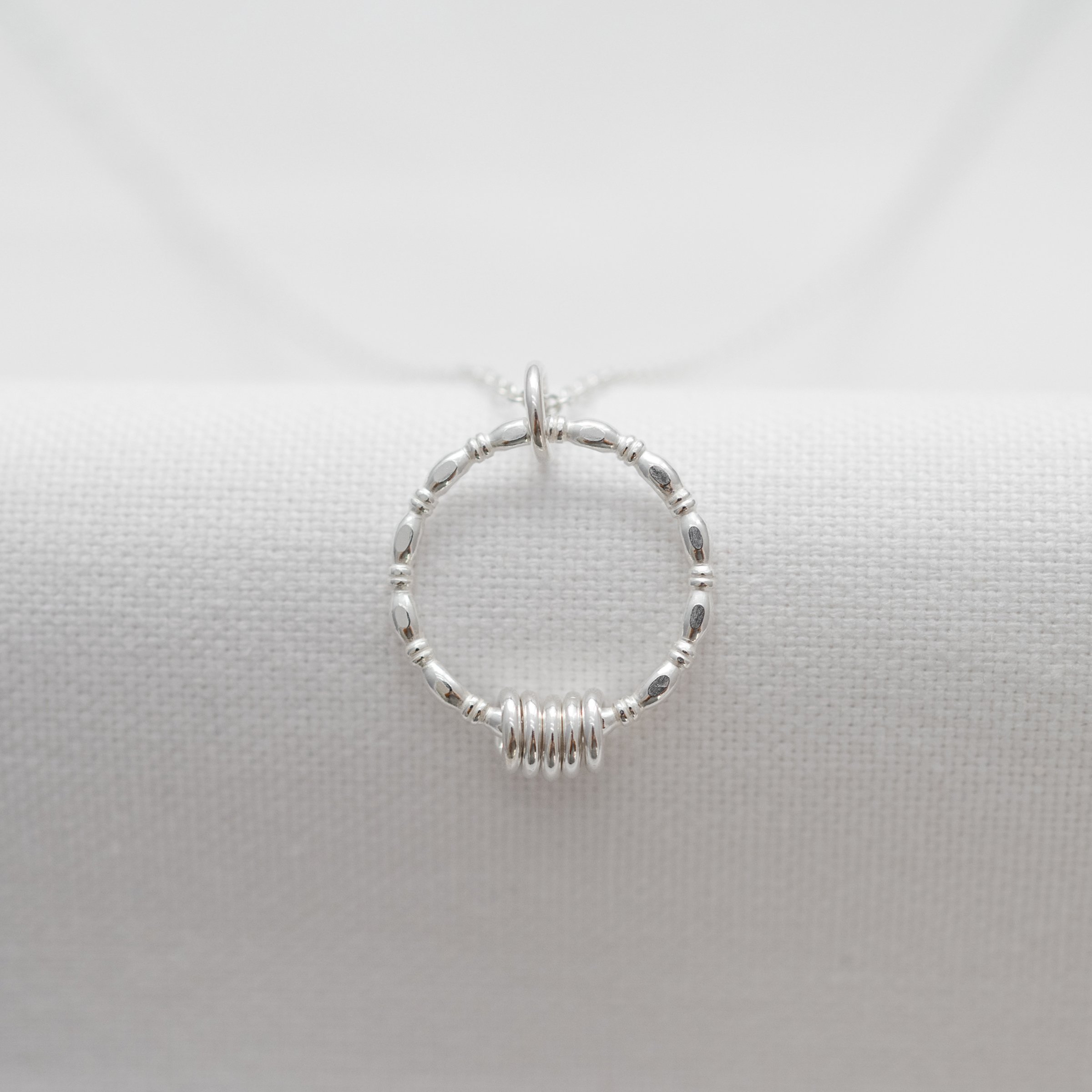 A front view of a silver 50th birthday necklace hanging over white material.
